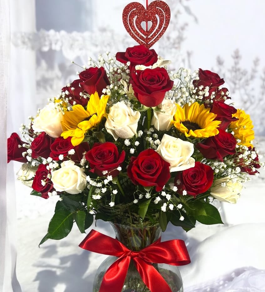 Sunlit Celebration - Celebrate in style with this vibrant and joyful floral arrangement! Featuring a stunning mix of deep red and creamy white roses, radiant sunflowers, and delicate baby's breath, this bouquet is designed to bring warmth and happiness to any birthday celebration. Accented with a classic red satin bow, this arrangement is the perfect gift to brighten someone's special day with love and cheer.
