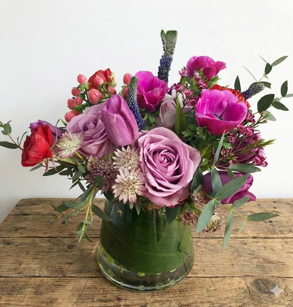 Designer's Choice-special day - Beautifully handcrafted bouquet designed especially by our floral experts for your special day. Arranged in a pinched, clear vase with a wide green leaf wrapped around the inside of the vase for an extra special touch. The arrangement stays in purple and pink color scheme. Flowers will vary based on availability and season – but don’t worry, we’ll make them extra special for your occasion! Standard size pictured. Larger sizes available.