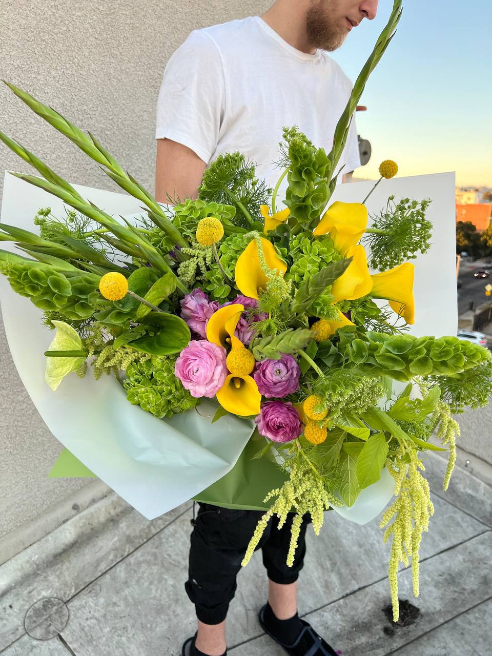 Emily - “Emily” – a bouquet filled with lightness, sunshine, and natural harmony.  Bright yellow calla lilies shine like rays of sunlight, weaving through delicate pink ranunculus, creating an atmosphere of joy and warmth. The lush greenery adds a fresh, natural touch, reminiscent of a summer garden bathed in the morning light. This bouquet combines elegance, airiness, and vibrant energy, making it the perfect gift for someone who deserves a moment of happiness.  “Emily” is a symbol of joy, inspiration, and the beauty of nature.