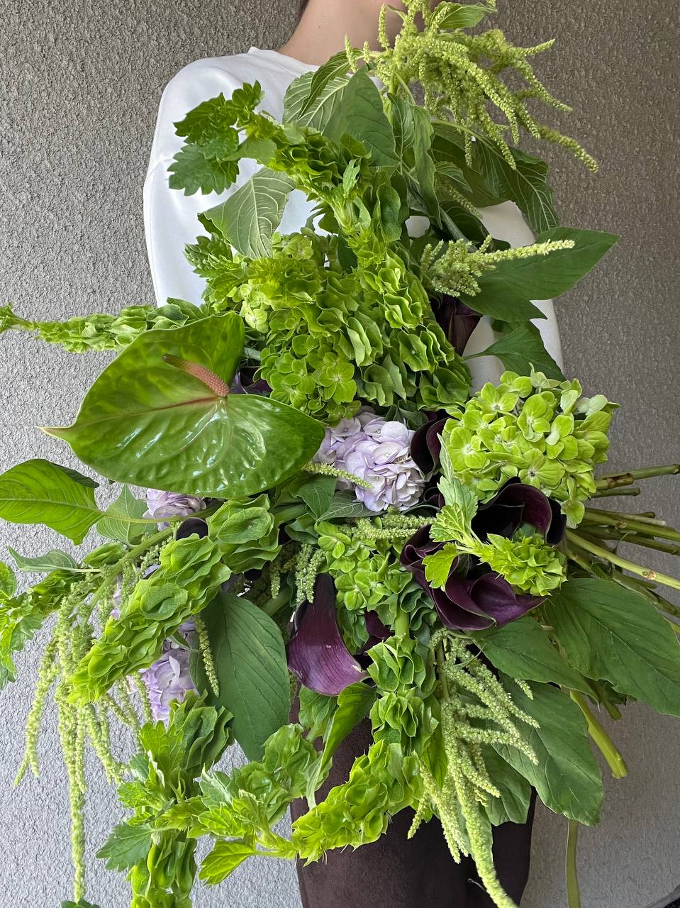 Woodland - Woodland is the breath of nature captured in an elegant bouquet. A lush blend of emerald greenery, soft textures, and deep purple calla lilies evokes the magic of a forest stroll. Cascading amaranthus adds graceful movement, while delicate lavender hues mirror the morning mist over a woodland clearing.  “Woodland” — where nature inspires beauty.