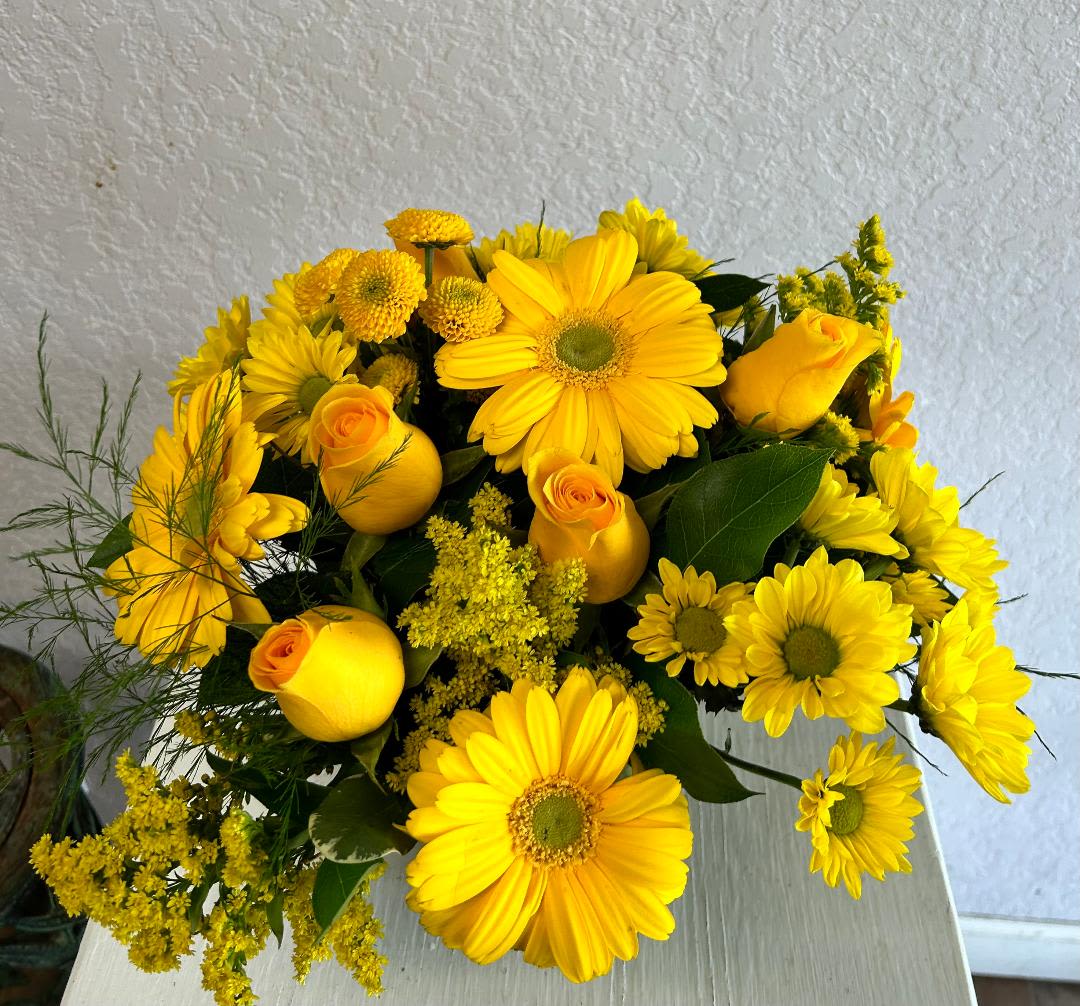 V129 - A low compact arrangment of mixed flowers in tones of yellow such as roses, daisies and other beautiful flowers. 