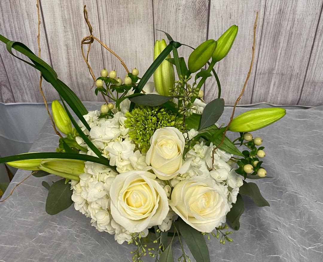 V127 - A low compact arrangement of high end white and green flowers such as roses, lilies, hydrangeas and other beautiful flowers. 