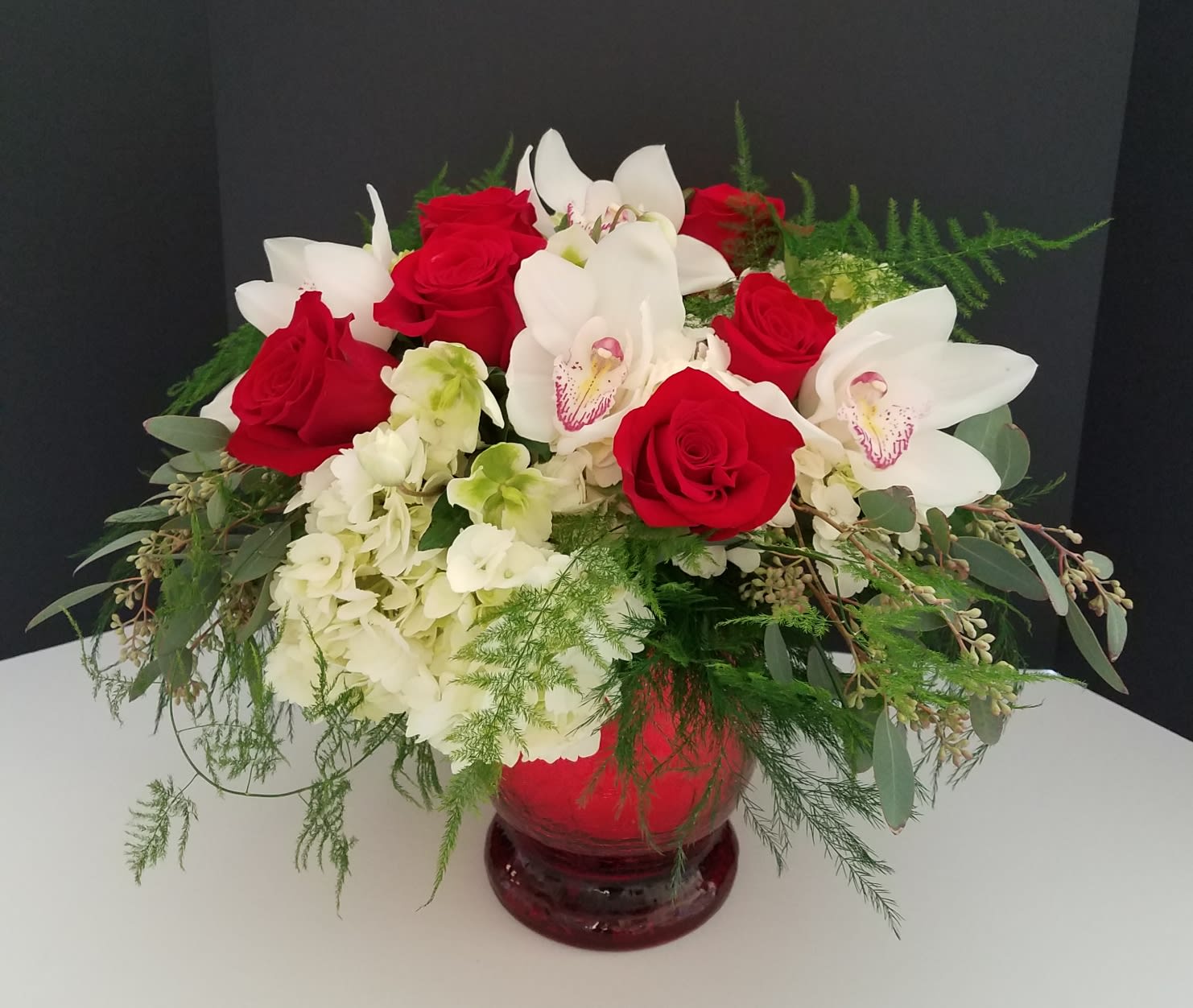 Isn't Love Grande - This gorgeous showstopper comes in a large red crackle vase and is filled with white hydrangea, red roses, green hellebores, white cymbidium orchids and finished with soft, romantic greenery.