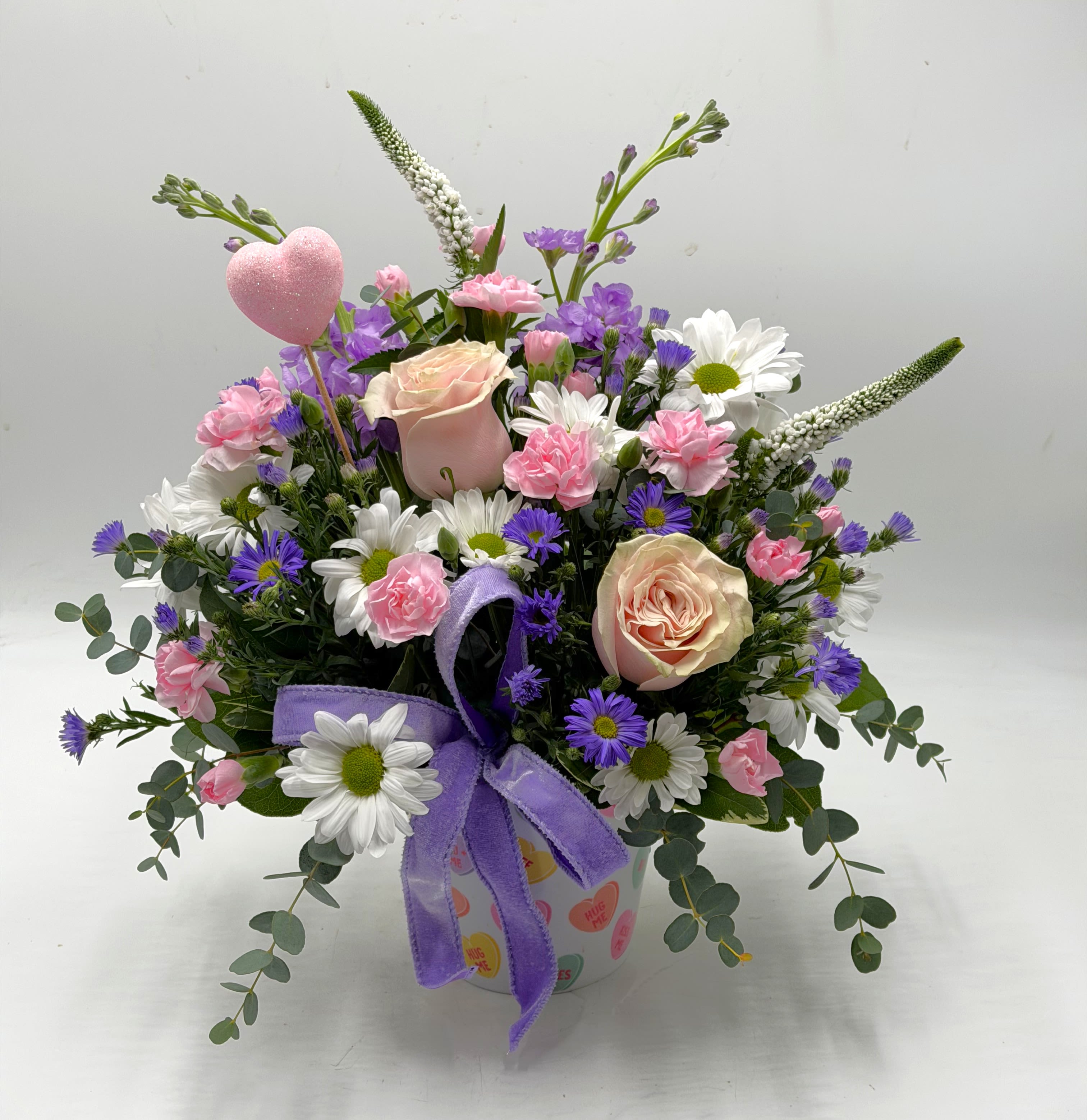 Valentine Meadow - Celebrate love with soft blush roses, sweet pink carnations, white daisies and pops of lavender designed in a ' Convo Heart ' container. 