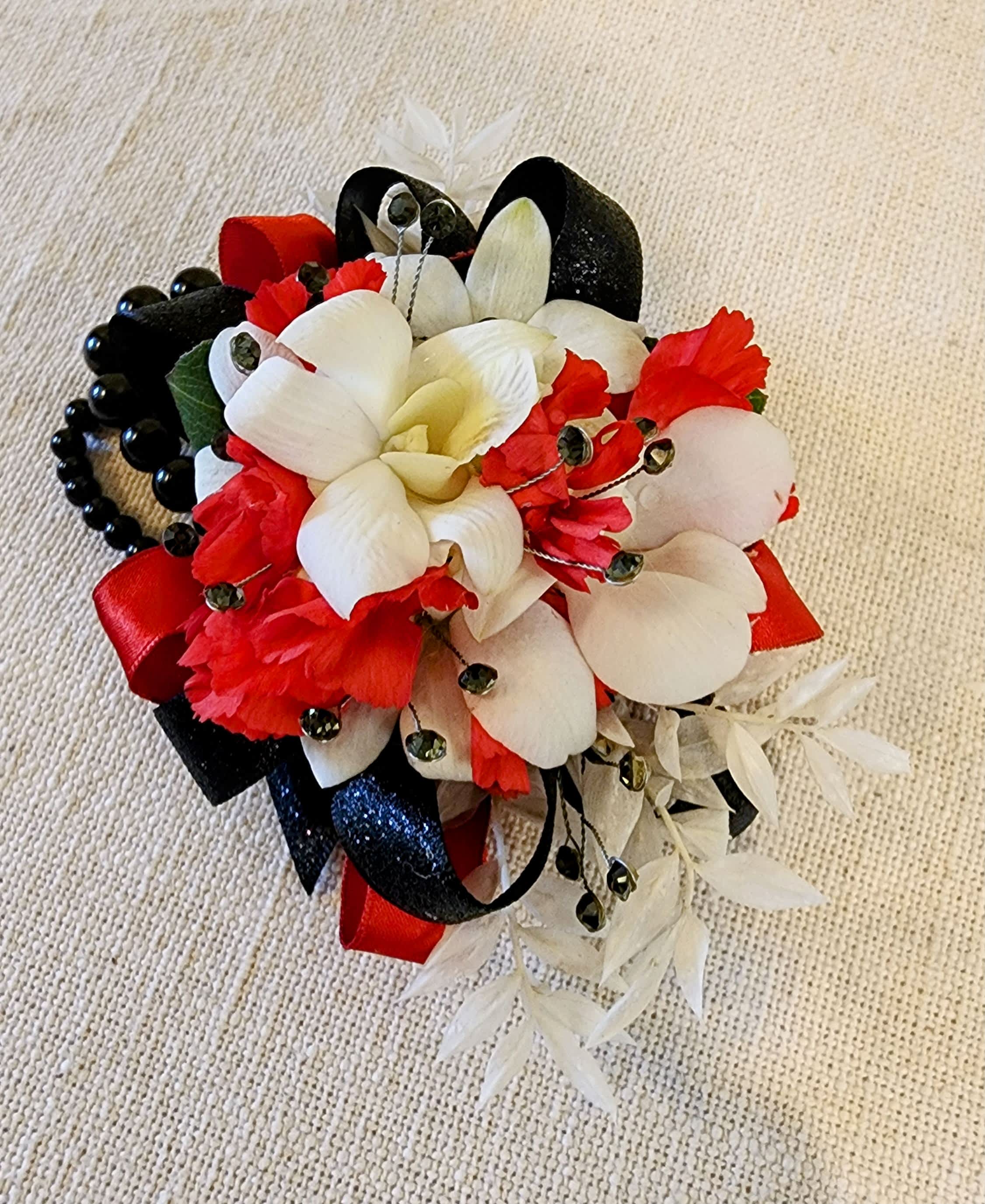 Corsage: Red, White &amp; Black wrist corsage - The red, white, and black wrist corsage is a striking accessory for formal events, featuring red roses or carnations, white orchids or lilies, and black ribbon or beads. The colors symbolize love, elegance, and modernity. Secured with an elastic band, it complements various dress styles, adding drama and flair to any occasion.