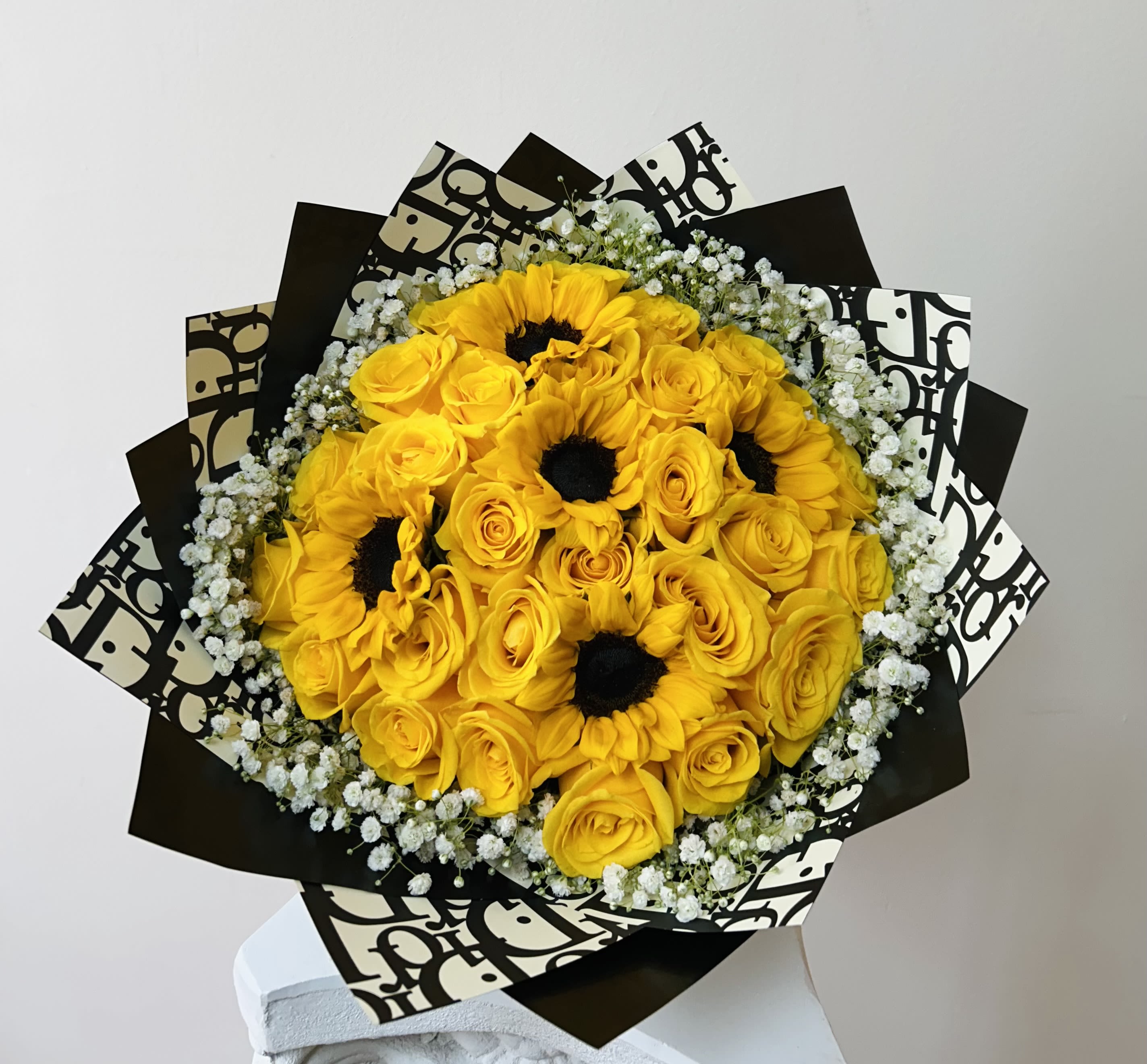 Yellow roses &amp; sunflowers - A radiant design that expresses joy and energy. Fresh yellow roses combined with a bright sunflower, symbol of light and vitality, enhanced with the delicate white touch of baby breath. An elegant and colorful detail to give happiness on any occasion.