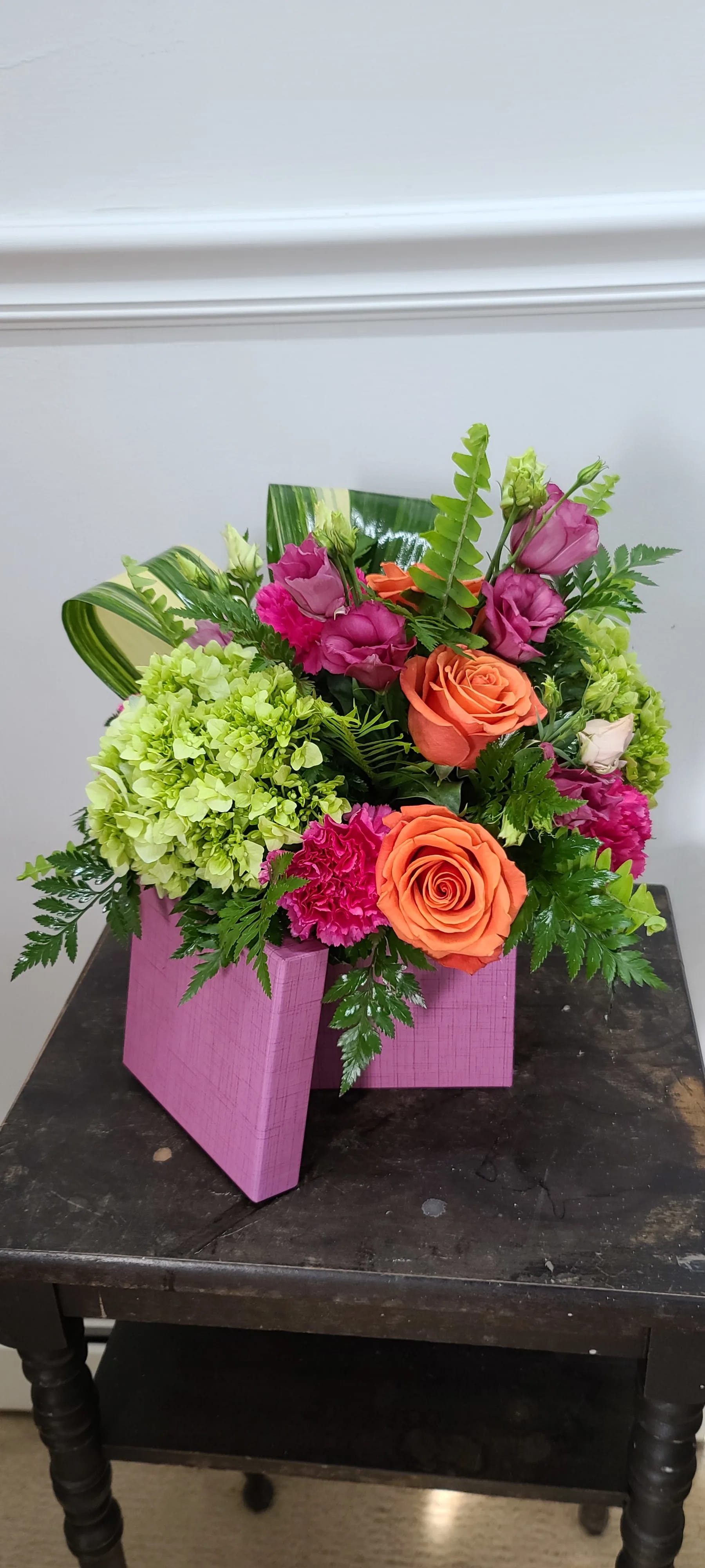 Love in the tropics - Bright, bold colors of orange, green and hot pink evoke thoughts of summer and warm weather. Long lasting hydrangea, roses, mini carnations, and lisianthus in our 4 x 4 mini hat box is easy to put anywhere and will brighten any room.   Deluxe upgrades to our 5 x 5 box and includes more roses and carnations. 
