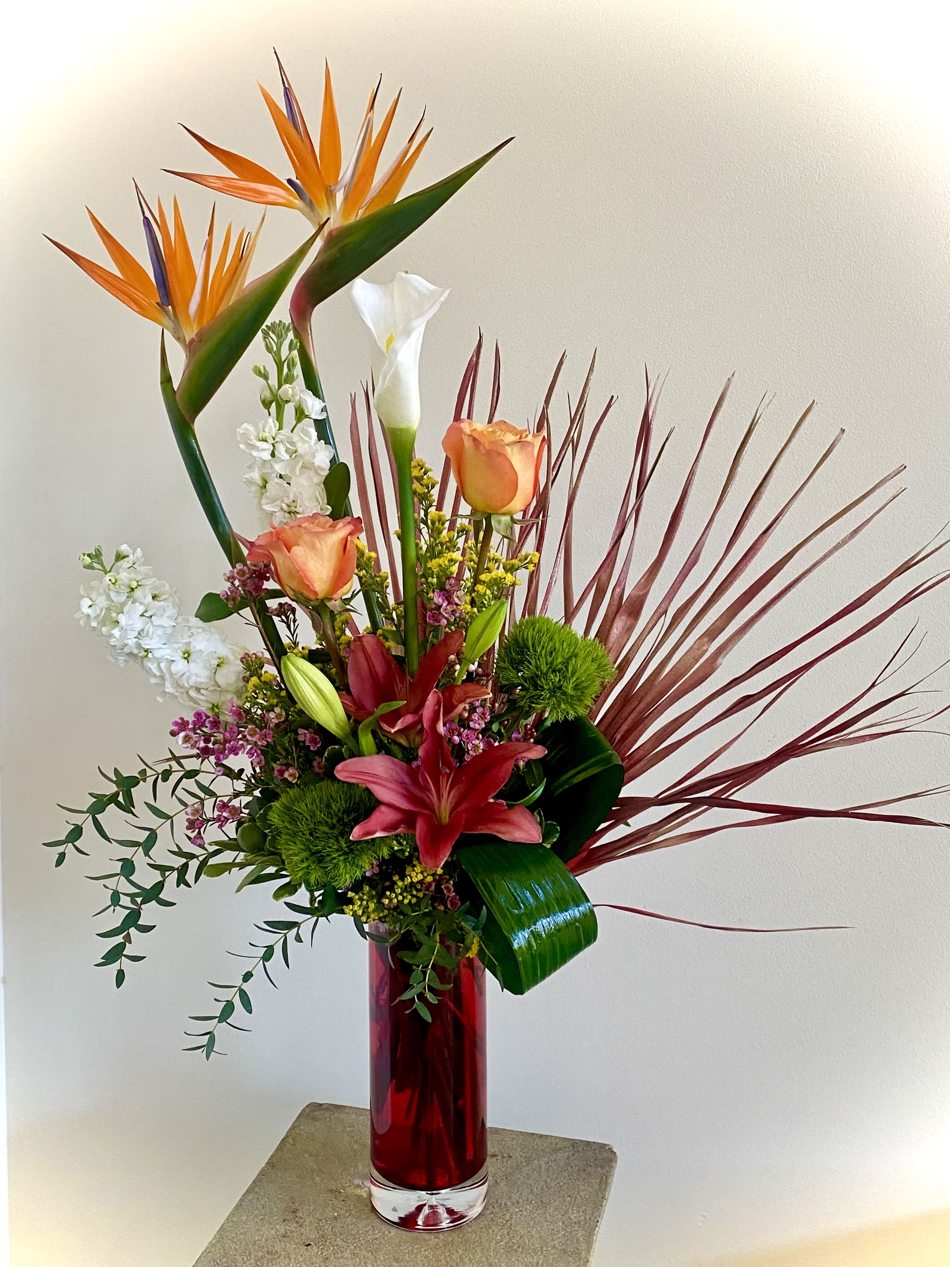 Valentine's Love in Paradise - Valentine's Love in Paradise is a gorgeous and unique design featuring a mix of tropical and garden flowers that is sure to impress! Featuring Bird of Paradise, Calla Lily, orange or yellow Roses, Palmetto Palms,  Stock and accented unusual tropical foliage. Stands approximately 35 inches tall.