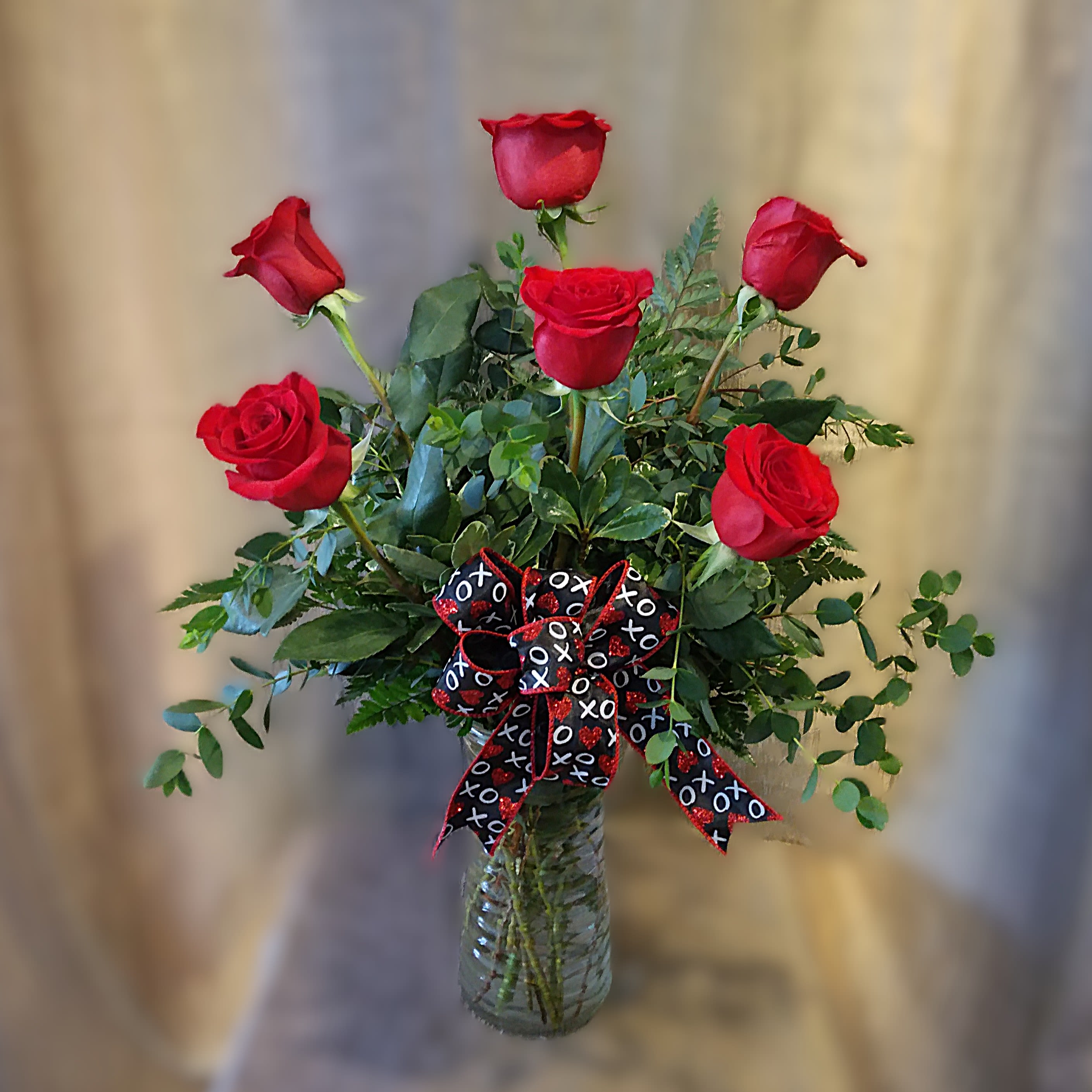 Valentine's Day Half Dozen Red Roses - PREORDER - 6 Elegant Red Roses in a clear glass rose vase with a festive bow! This luxurious arrangement features 6 of the finest long-stemmed red roses, expertly arranged with lush foliage to showcase their natural beauty and grace. The rich red hue of the roses symbolizes deep love, passion, and admiration, making it the perfect gift to express your love and appreciation.  Available after 02/06/2026 