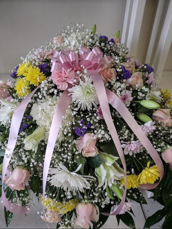Beautiful Mix Assorted Flowers Casket Spray - A beautiful mix of pink/white roses, yellow/whit carnations, purple delphinium, baby's breath, tied together with lush greenery. A beautiful tribute for your loved one.
