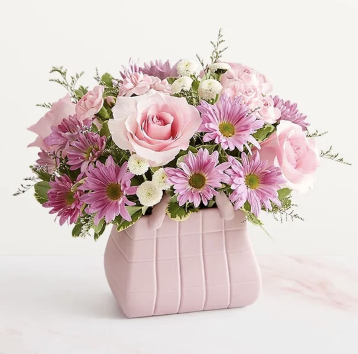 Designer Dreams Bouquet - The ultimate arrangement for your favorite fashionista. A profusion of roses, poms, and other blooms all but spill out of the top of our keepsake handbag-shape vase, making this a truly chic gift. And just like the perfect handbag, the pink, white, and lavender bouquet goes with just about everything.