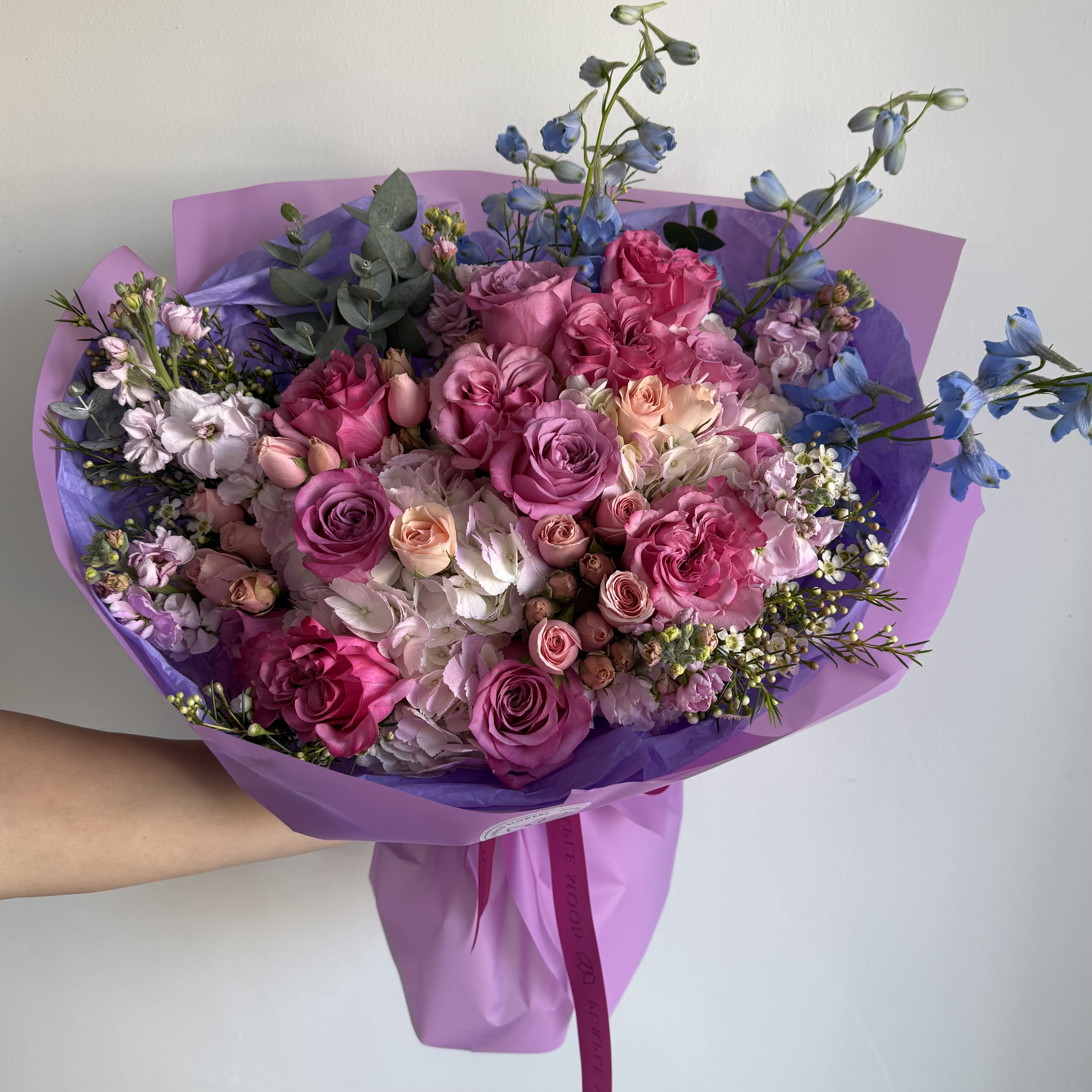 Plum Bouquet - Plum Bouquet Rich, vibrant, and full of charm — the Plum Bouquet is a dazzling mix of purples, pinks, and soft pastels, wrapped in elegant lavender paper. Its playful yet sophisticated palette makes it the perfect choice for gifting joy, romance, or celebration.      •    A lush mix of roses, lisianthus, hydrangeas, and seasonal blooms     •    Wrapped in elegant lavender paper with a matching ribbon     •    Available in Standard, Deluxe, and Premium sizes     •    Perfect for birthdays, anniversaries, or simply to brighten someone’s day  VASE NOT INCLUDED