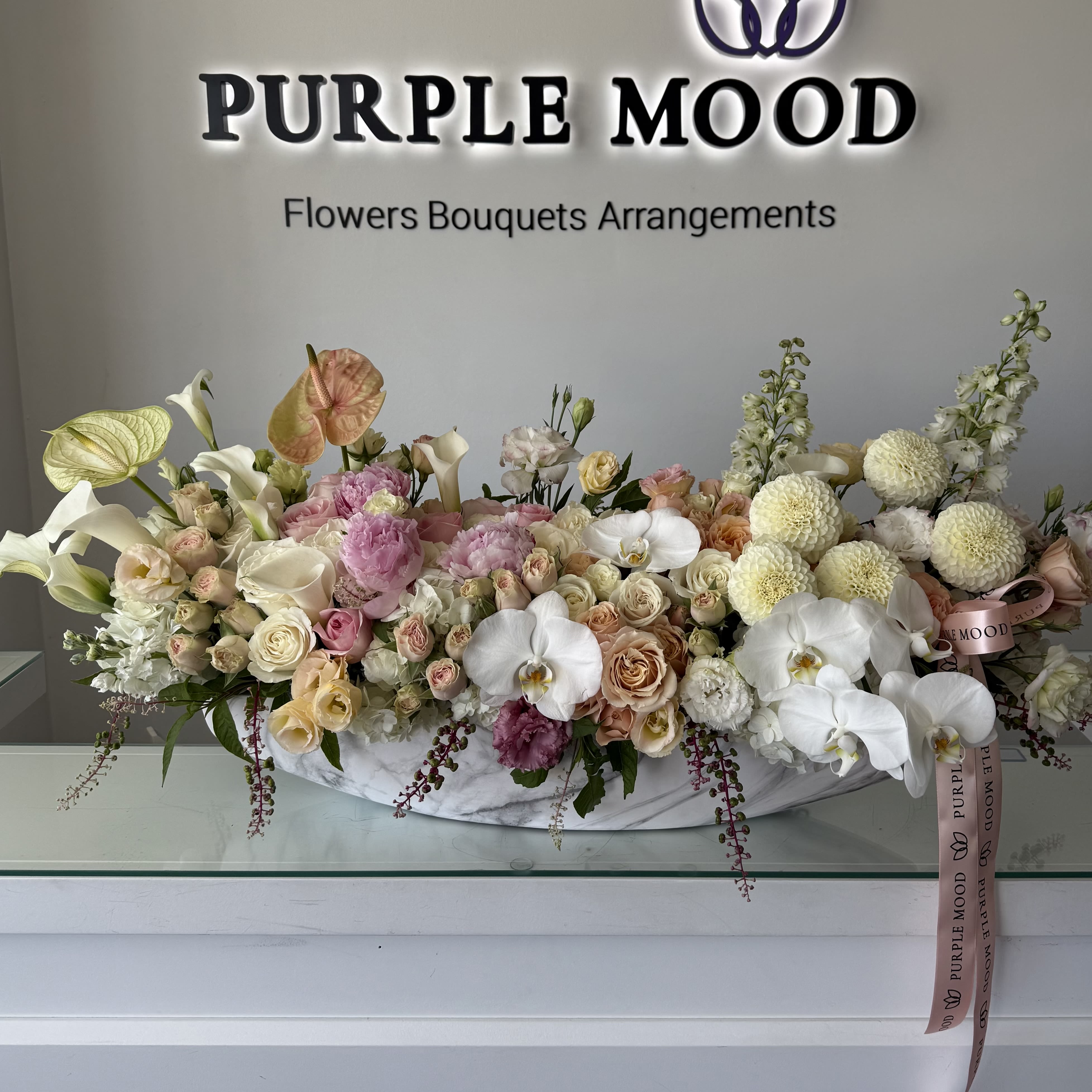 Grand Vase - Make an unforgettable statement with the Grand Vase — an extra-large luxury arrangement overflowing with color, texture, and elegance. Designed in an elongated white vase, this masterpiece blends exotic orchids, calla lilies, and roses with lush seasonal blooms in soft pastel tones. Perfect for weddings, galas, or impressing someone truly special, this piece transforms any space into pure luxury.  Key Features:     •    Extra-large size for maximum impact — a true centerpiece arrangement     •    Styled in a sleek elongated vase for a modern, elegant look     •    Perfect for weddings, grand events, or extraordinary gifting     •    A luxury statement piece designed to wow at first sight