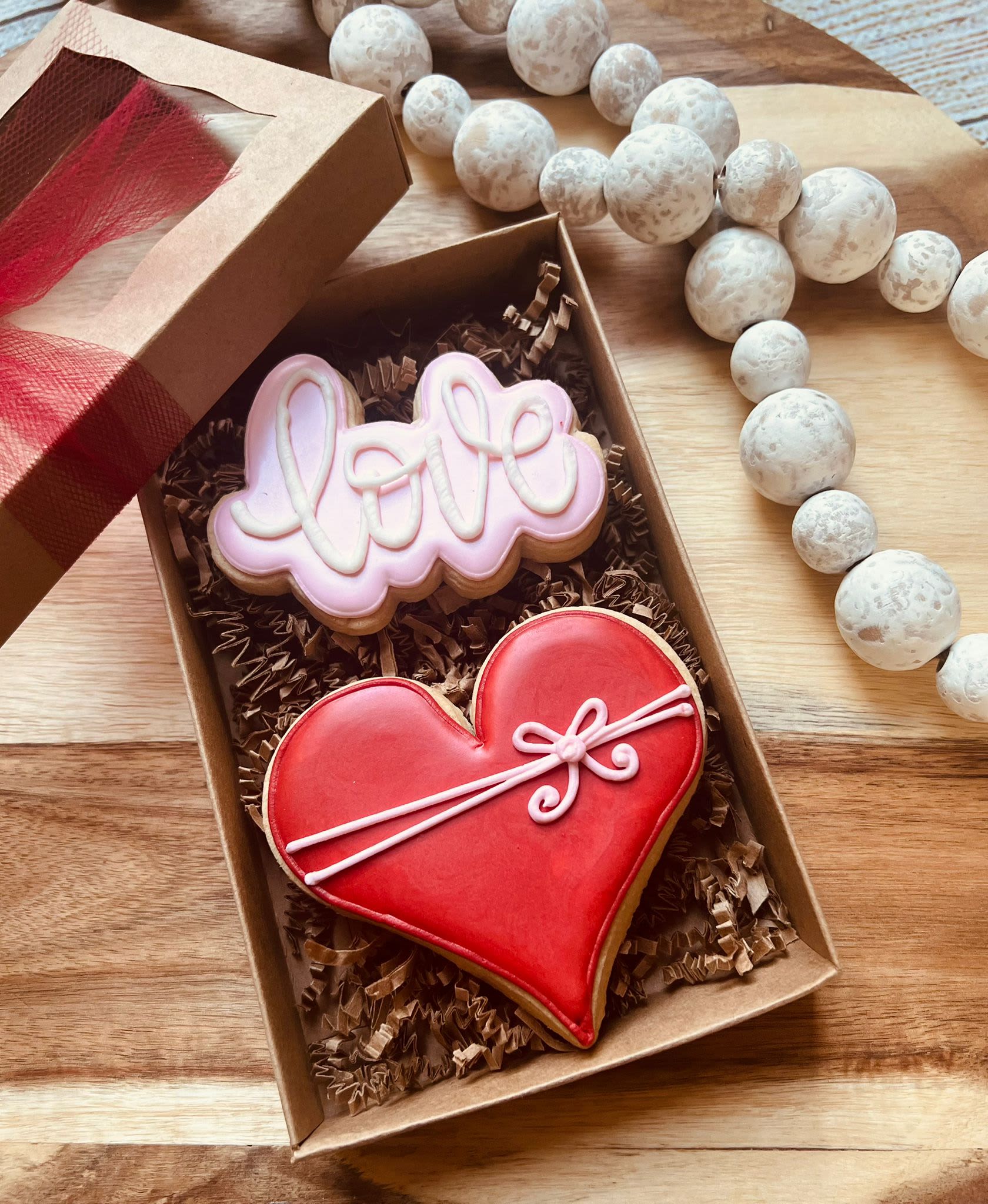 Valentine’s Day Luxury Duo by The Sugar Jar, Exclusively by Ana  - 1. Pink &amp; White LOVE Cookie Handcrafted sugar cookie spelled out in bold letters, iced in soft pink and white hues. Delicate piping accentuates each letter, making the word “LOVE” truly stand out. Perfectly balanced sweetness and a melt-in-your-mouth texture. Red Heart Cookie  2. Classic heart-shaped cookie in a vibrant, romantic red. Smooth royal icing finishes each heart with a glossy sheen. Ideal for sharing (or keeping all to yourself). Why They’re Special  Each cookie is individually handcrafted with premium ingredients and meticulously decorated to capture the spirit of Valentine’s Day. Presented in an elegant gift box, complete with a ribbon—ready to surprise someone special. An exclusive creation from The Sugar Jar by Anna, ensuring you get a one-of-a-kind treat that looks as exquisite as it tastes. Add these luxurious cookies to your Valentine’s Day celebration and sweeten the occasion in style.  facebook.com/thesugarjar instagram.com/thesugarjarhouston/