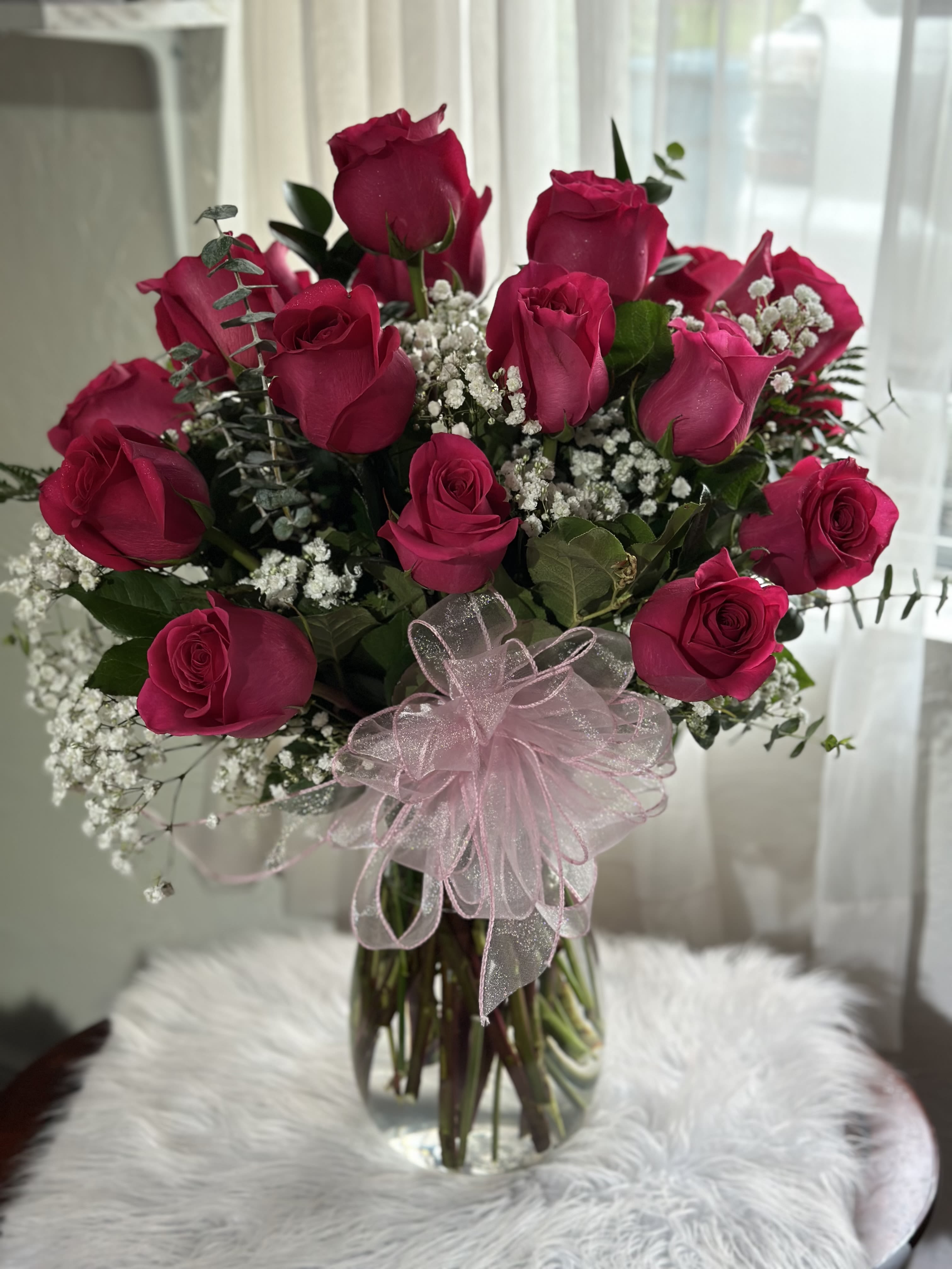 Bonita Bouquet - 24 hot pink roses, baby breath and greens foliage in a clear glass vase.