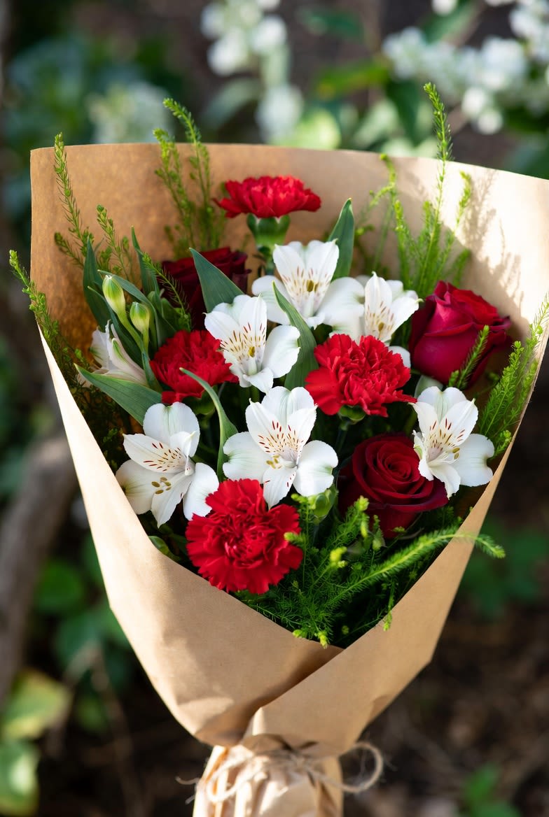 Crimson &amp; Ivory – Hand-Wrapped Bouquet - A timeless classic wrapped in rustic kraft paper: bold red carnations and velvety deep red roses mingle with crisp white alstroemeria for striking contrast and lasting freshness. Lush greens add natural volume and a just-picked-from-the-garden feel. Simple, elegant, and effortlessly romantic—this bouquet is perfect for anniversaries, "thinking of you," or a heartfelt everyday surprise.  