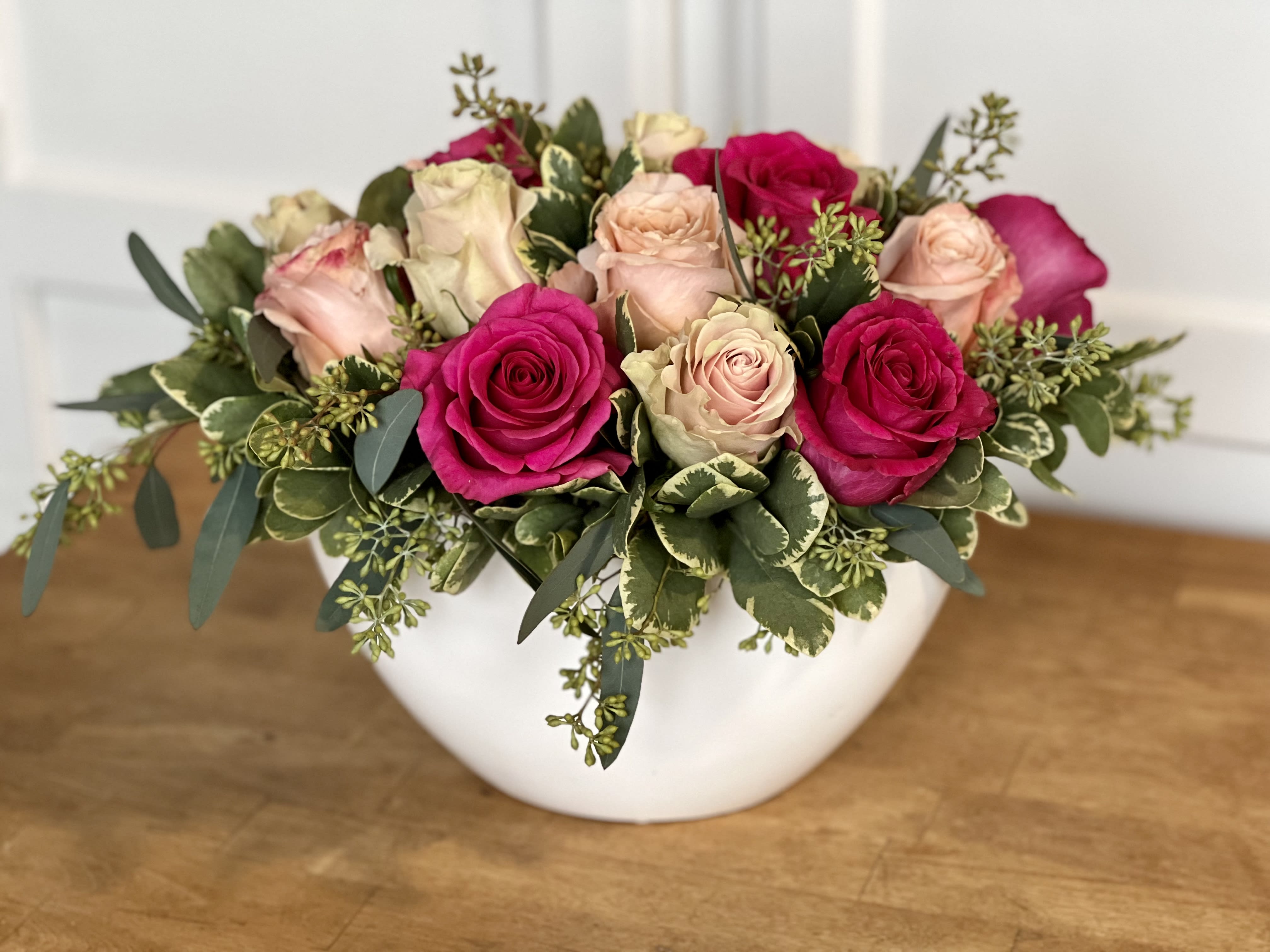 Lovespell - A low, lush, elegant arrangement of 15 assorted pink roses in a white ceramic crescent-shaped vessel.