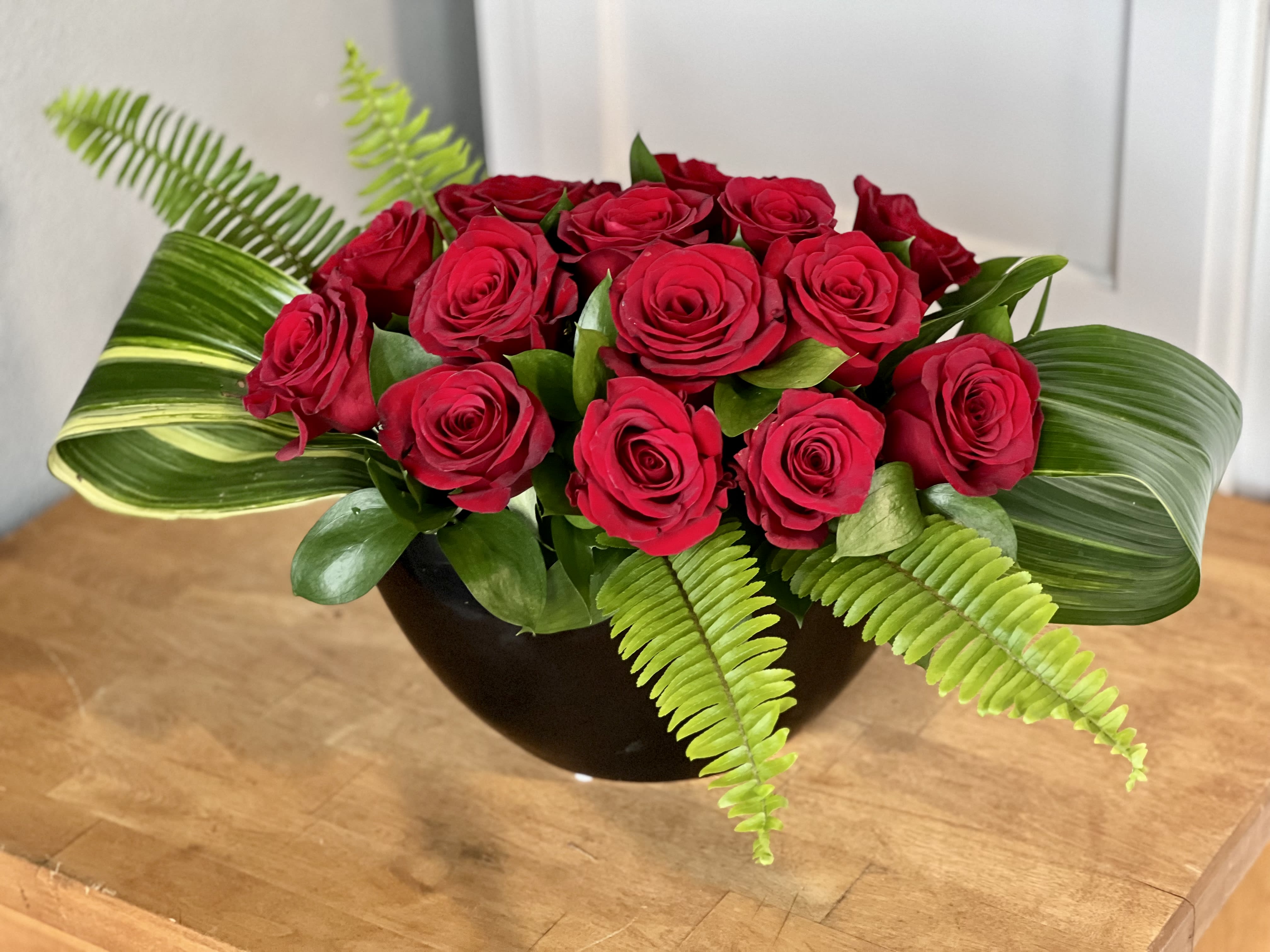 Moonstruck - A sleek and elegant modern arrangement of 15 red roses in a black ceramic crescent shaped vessel. Arrangement is a medium size.