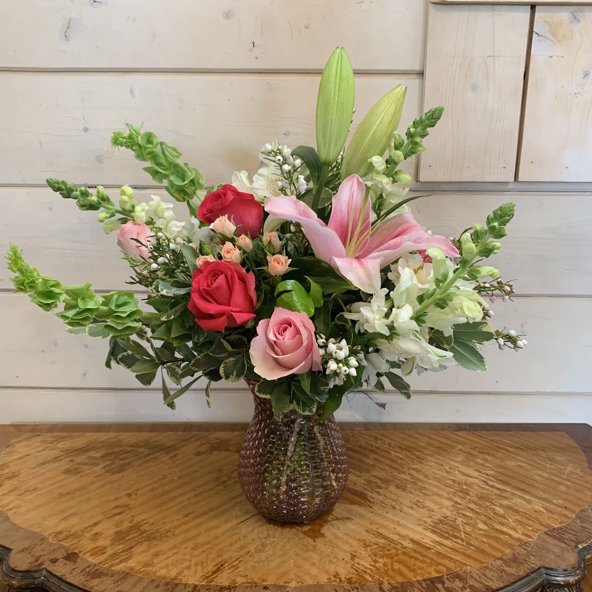 Mom's Rose Bouquet - Hot pink roses, light pink roses, and light pink spray roses with dancer lilies, white snapdragons, and bells of Ireland in a pink glass hobnail posy vase with white alstroemeria and Boronia. Approximately 16" high and 15" wide.