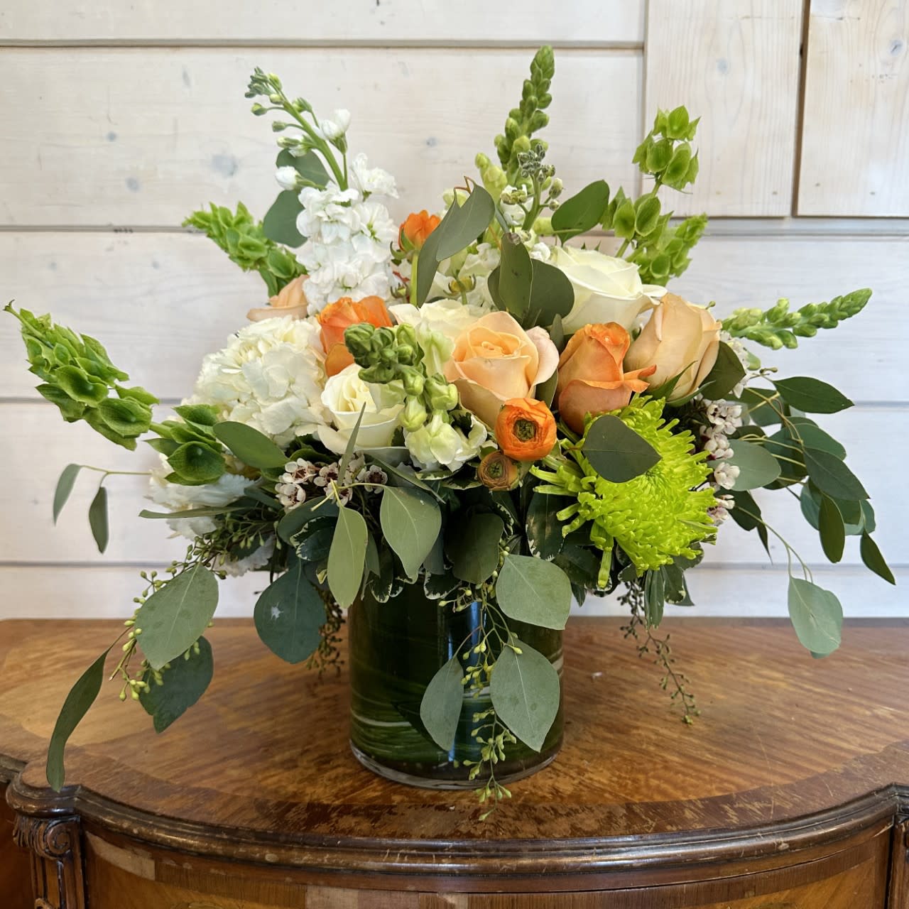 Creamsicle  - white hydrangea, white snaps, white stock, bells of Ireland, white roses, coral roses and peach roses, orange ranunculus and green chrysanthemums arranged in an extra large leaf lined round gather vase. Approximately 16in tall and 18 in wide..  