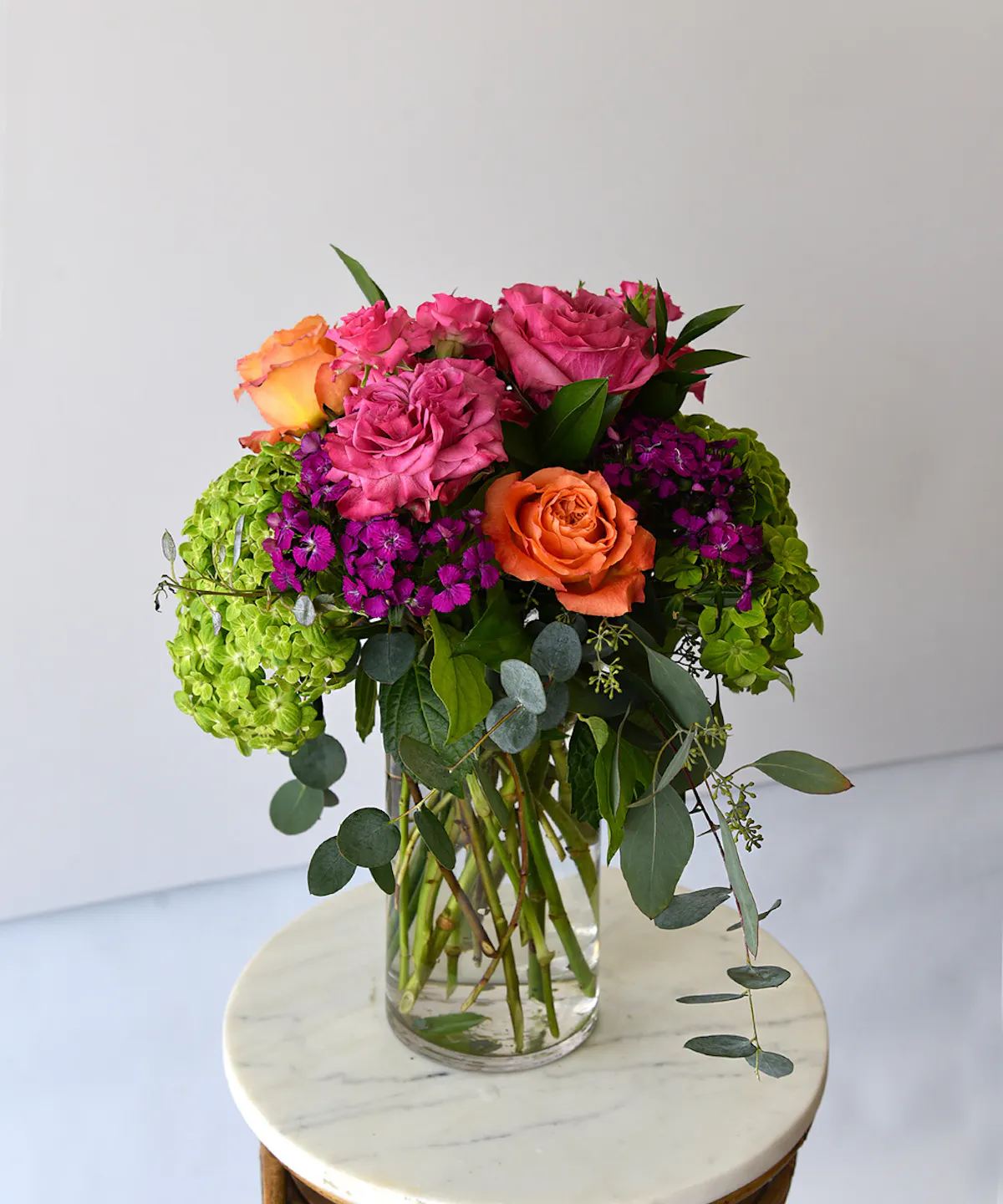COLOR ME ROSY - A beautiful collection of stunning premium roses with spray roses in vibrant hues of tangerine orange, ruffled mauve-pink rose and soft pink roses.  Accented with green hydrangea, seasonal blooms and foliage designed in a classic tall glass vase.  Simply lovely!