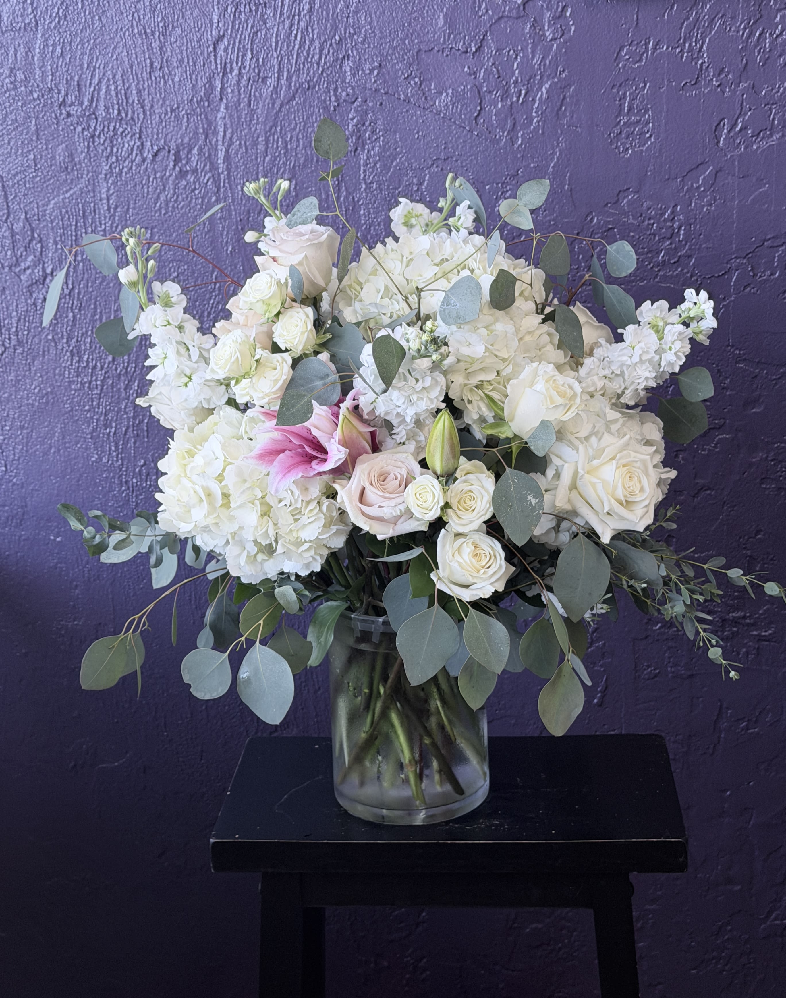 Breezy by the Ocean - Elegant and serene, this arrangement features white lilies, roses, and hydrangeas in soft shades of blue and cream. Designed in a clear glass vase, it’s perfect for any occasion — bringing freshness, grace, and peaceful beauty to any space.  in 10" glass vase