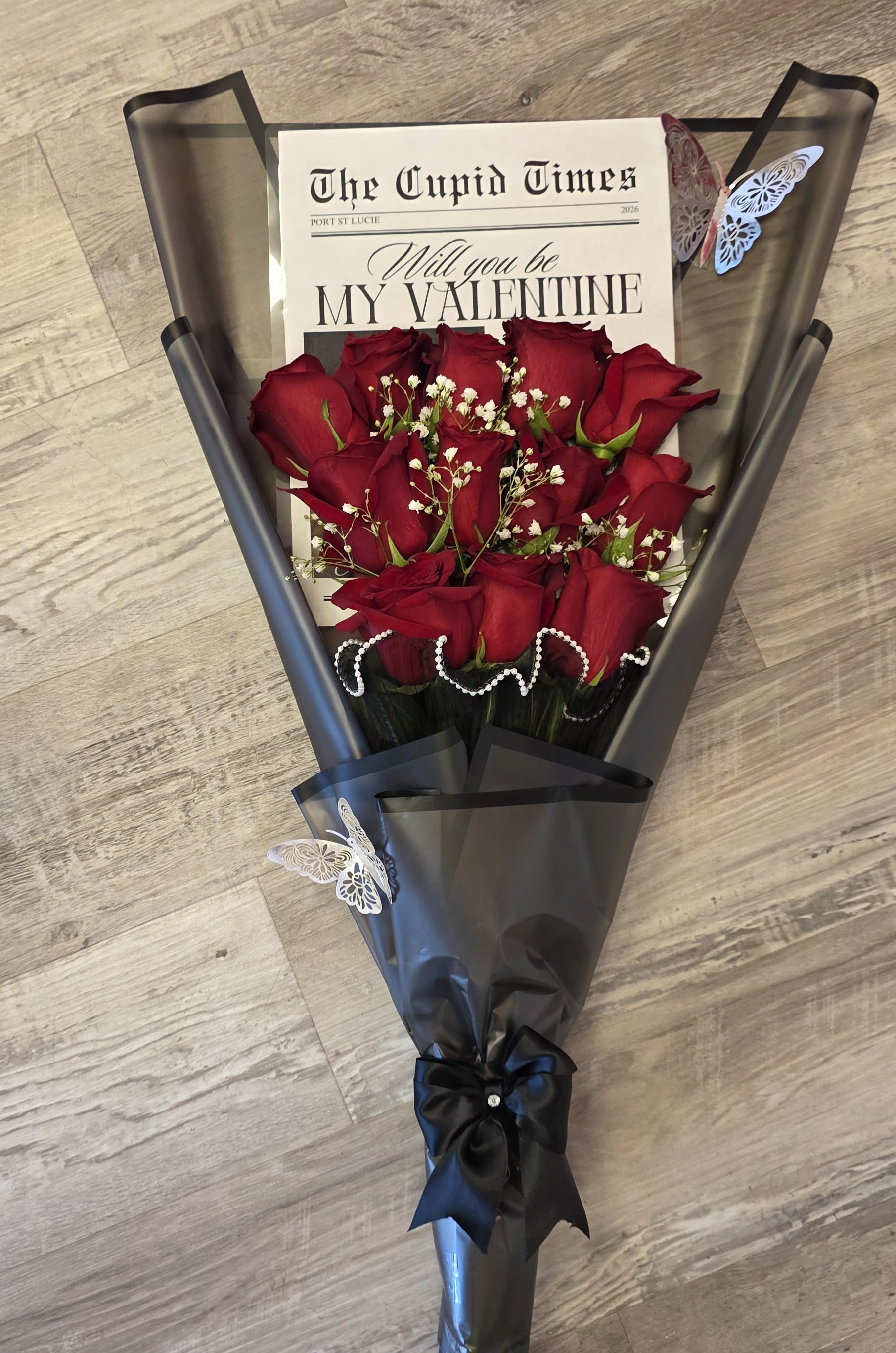 Be My Valentine - A dozen vibrant roses, elegantly arranged in newspaper print, with "Be My Valentine" message.