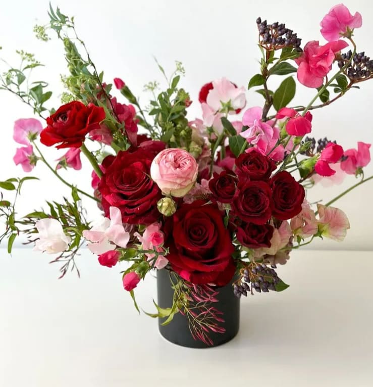 Foxy - A gorgeous gathering of deep red roses with touches of Italian Pink Ranunculus and Japanese Sweet pea in a whimsical design.