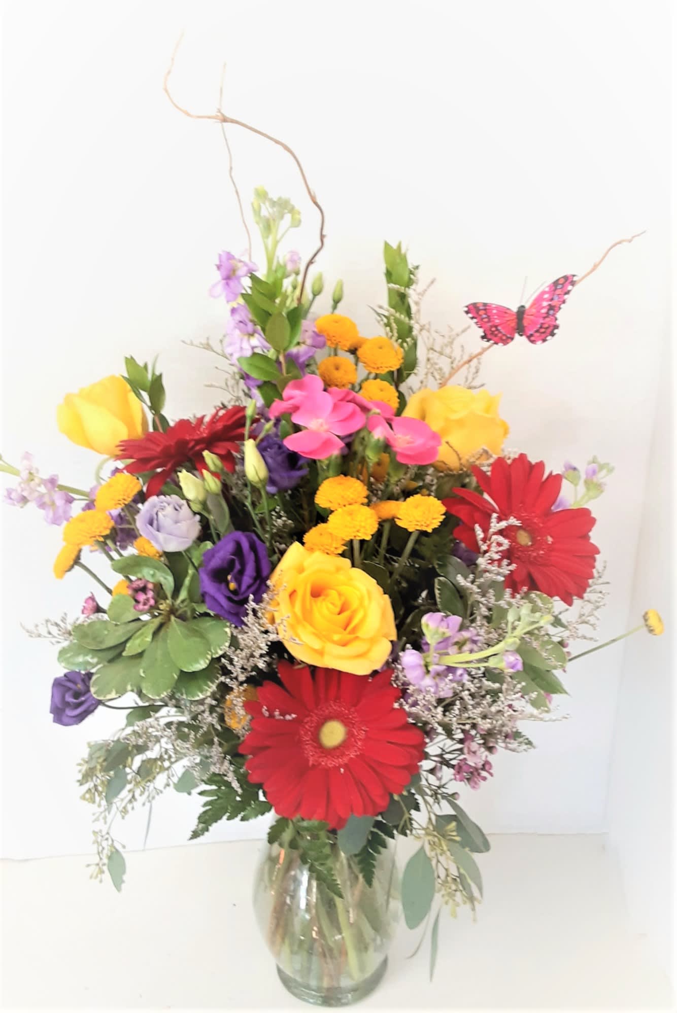 Colors - Roses,gerbera daisies,and an array of bright,mixed flowers with curly willow and a butterfly in a clear vase.Some flowers will vary.