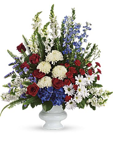 With Distinction - A dazzling display of patriotic red, white and blue flowers sends a silent yet poignant statement about hope, freedom and the strength to endure. This proud bouquet is a testament to life that is sure to be appreciated.  A beautiful mix of all-American red, white and blue flowers such as hydrangea, roses, miniature carnations, snapdragons, chrysanthemums and more are perfectly arranged in a white urn. Approximately 31" W x 34 1/2" H