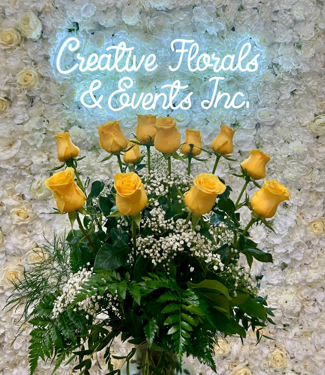 V130 - A dozen yellow roses arranged in a tall clear glass vase with mixed greenery and filler. 