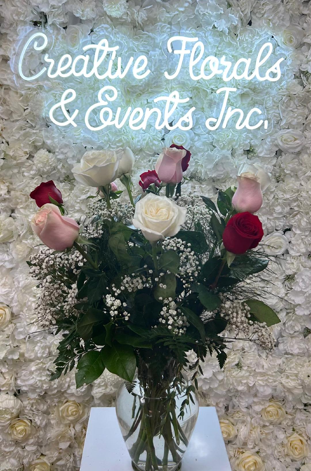 V124 - A dozen roses in pink, red and white arranged in tall clear glass vase with mixed greenery and filler. 