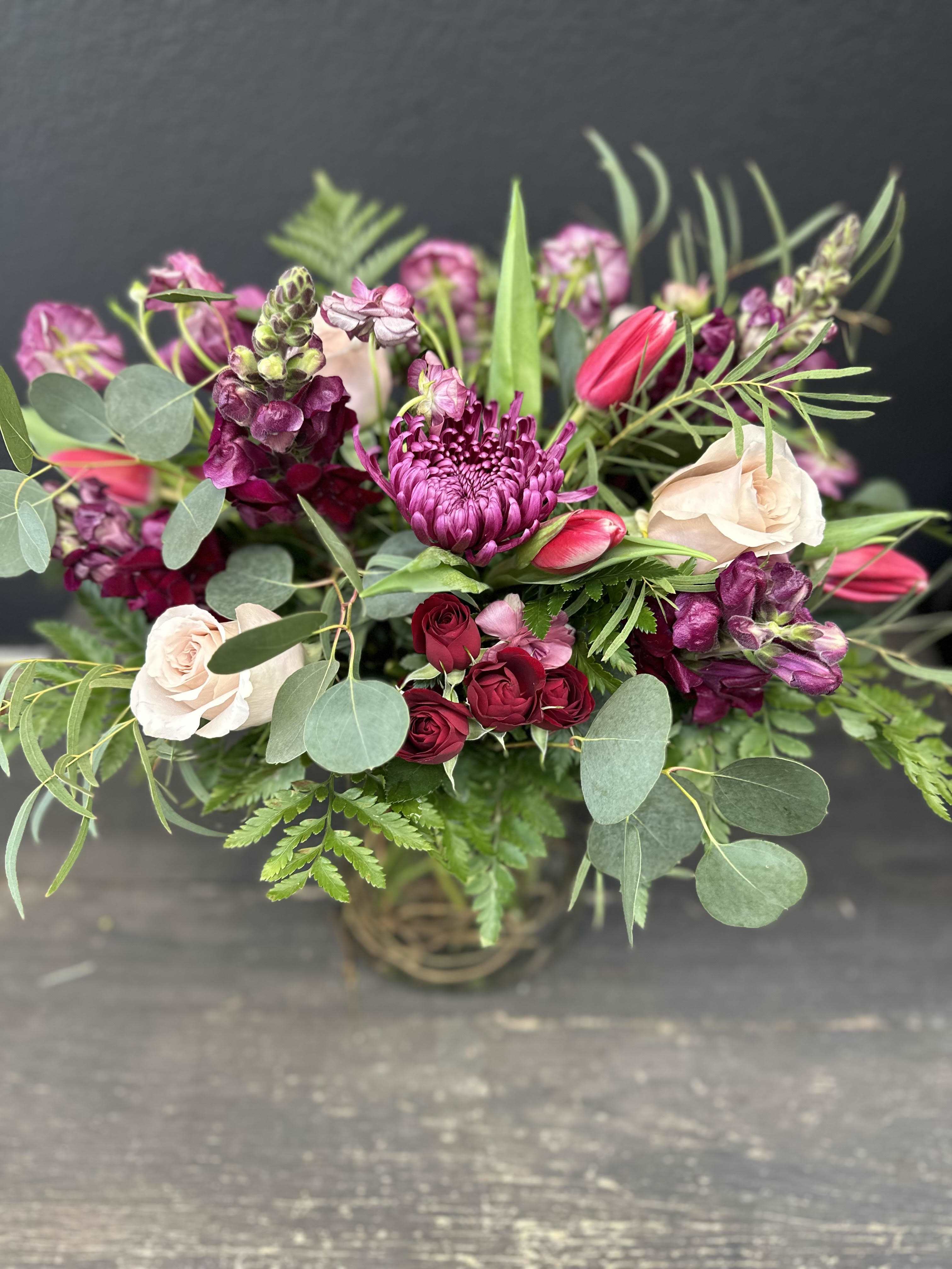 Mama Mia - Designed using burgundy mums, maroon snapdragons, dark red spray roses, blush roses, hot pink tulips, and mauve butterfly ranunculus, with eucalyptus foliage.