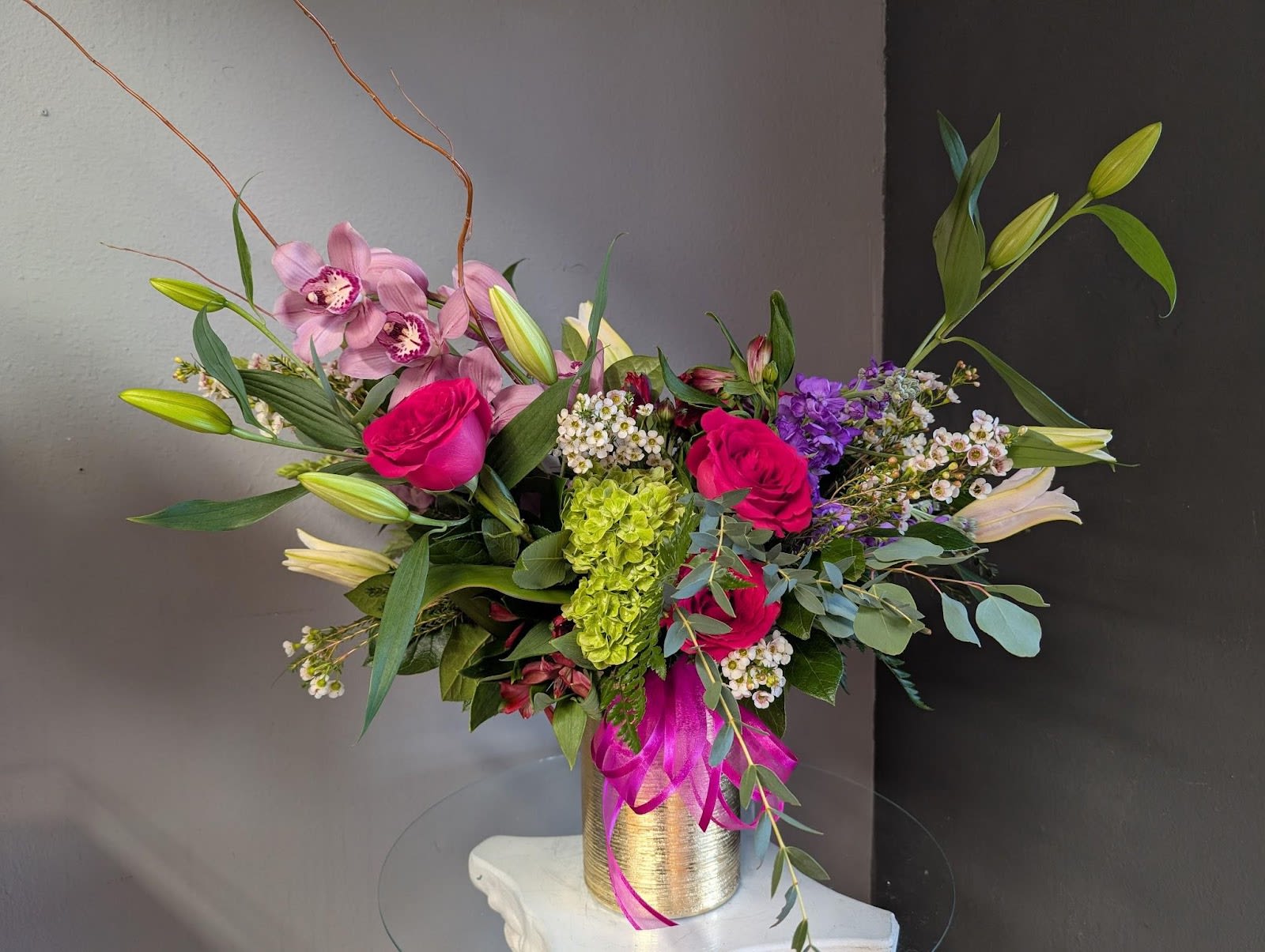 Gold Crush-- Valentine's Day Catalog - The brightest arrangement on our Valentine's Day catalog is a stunning mix featuring fresh flowers such as lilies, roses &amp; cymbidium orchids. A beautiful way to show that special someone just how special they really are. Flowers, greens and filler WILL all be hand chosen by the designer based on available stock and quality.  *PLEASE NOTE for Valentine's Day (2/12 to 2/14) **Bloomsnaps and timed deliveries are NOT available  (Due to the volume of orders, uploading photos will crash our system) ***Stock is based on availability and quality. Flowers, filler and vase will be chosen at the designers discretion. Quality is most important to us. ****ALL ARRANGEMENTS THAT ARE PICKED UP OR DELIVERED WILL LOOK DIFFERENT FROM THE PHOTO SHOWN.  