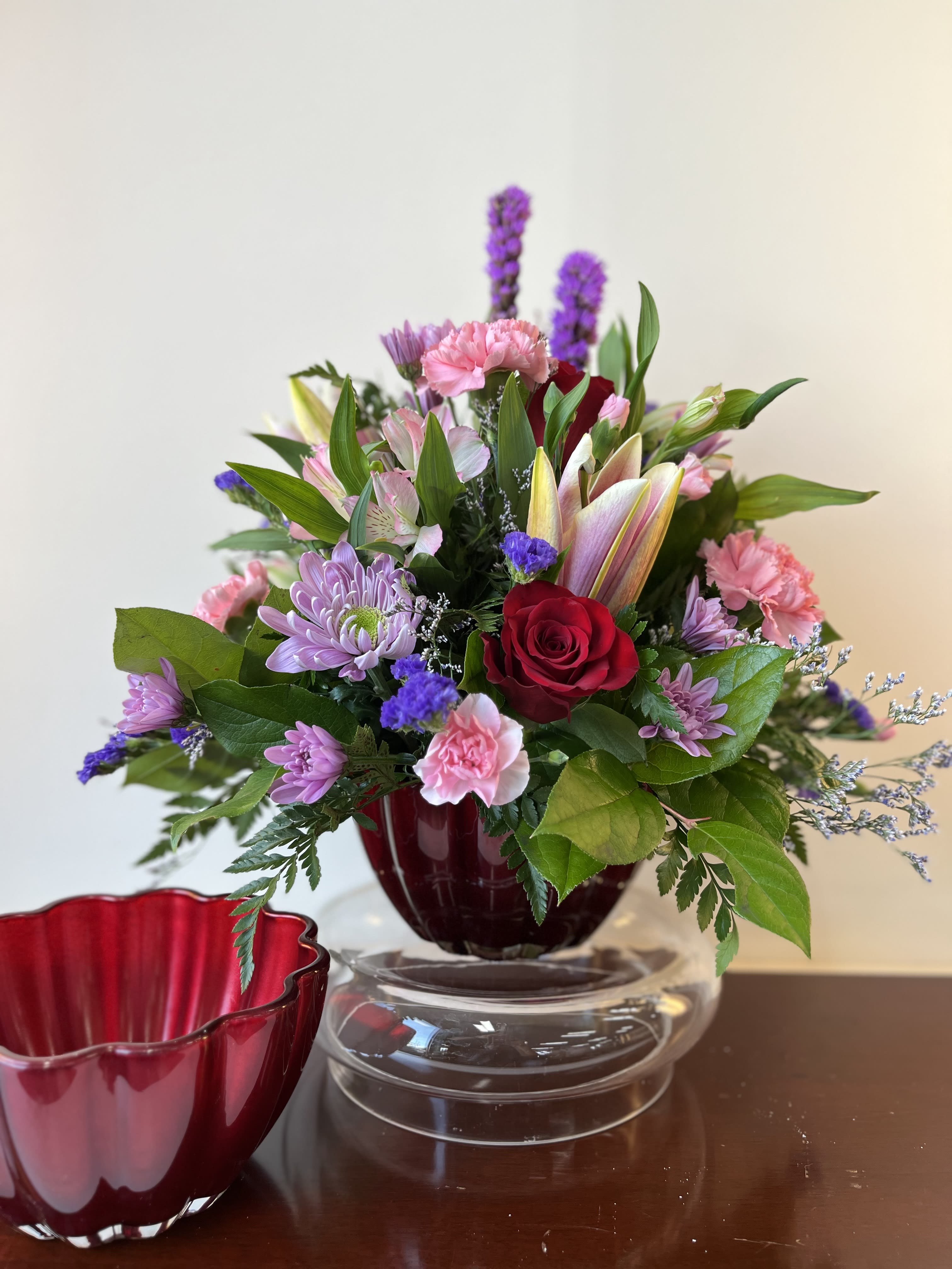 True Romance Bouquet - This stunning arrangement of seasonal blooms including roses and lilies is presented in a vibrant red keepsake bowl.  Perfect way to let that special someone that you love them.