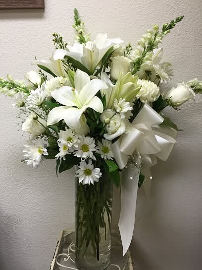 Let it Grow - Type of Flowers: White Roses, White Oriental Lilies, White Snapdragons, Daisies, Mums, and Greens in a tall clear cylinder cube vase with a white bow. Availability: All year round Substitute Availability: Yes
