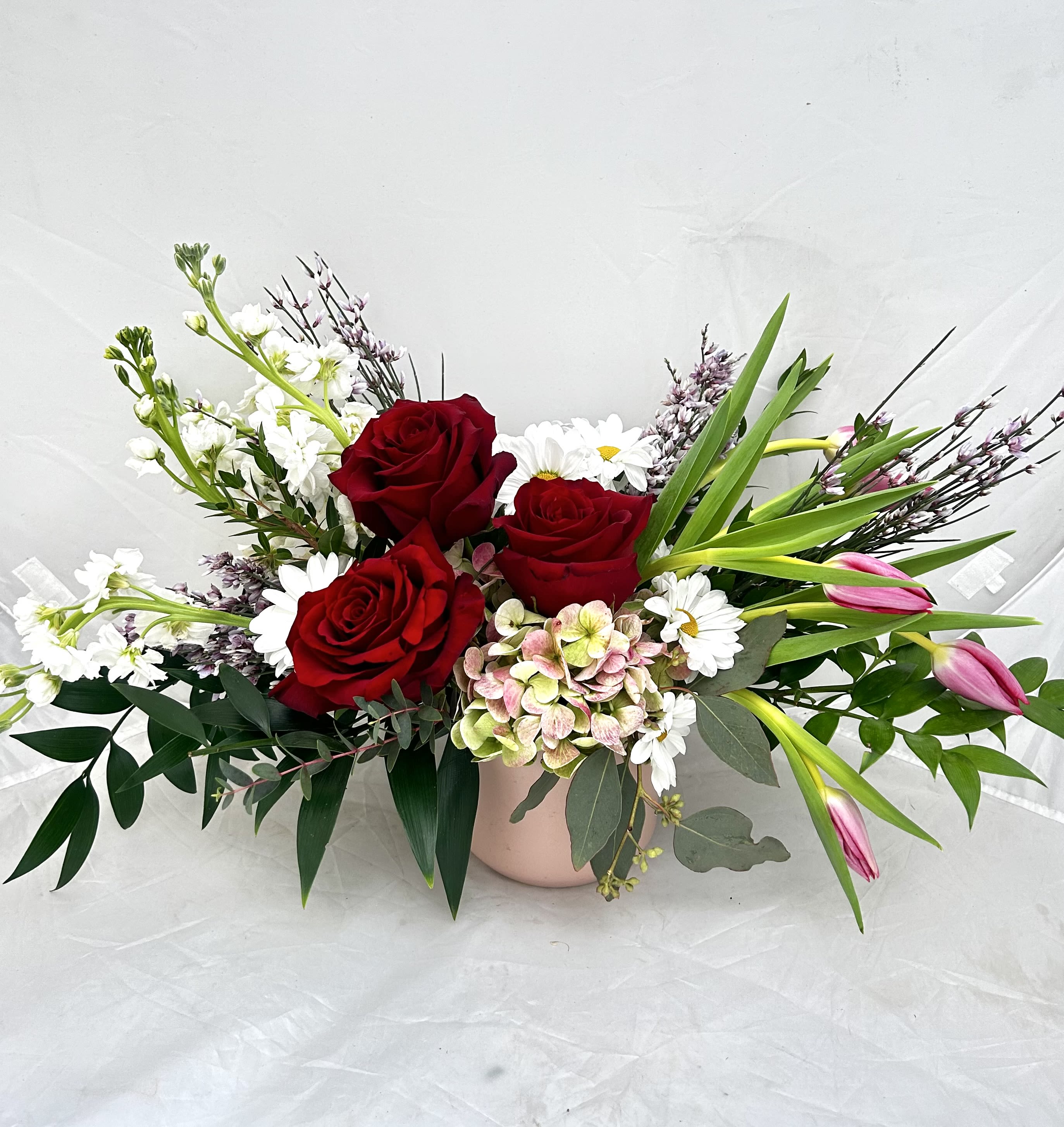 Graceful - Celebrate elegance with the Graceful bouquet, a stunning blend of deep crimson roses and delicate pink tulips. Accented with fresh white daisies, soft hydrangeas, and airy waxflowers, this arrangement is nestled in a charming blush-toned vase. It’s a sophisticated choice for birthdays, anniversaries, or simply to show someone they are on your mind.