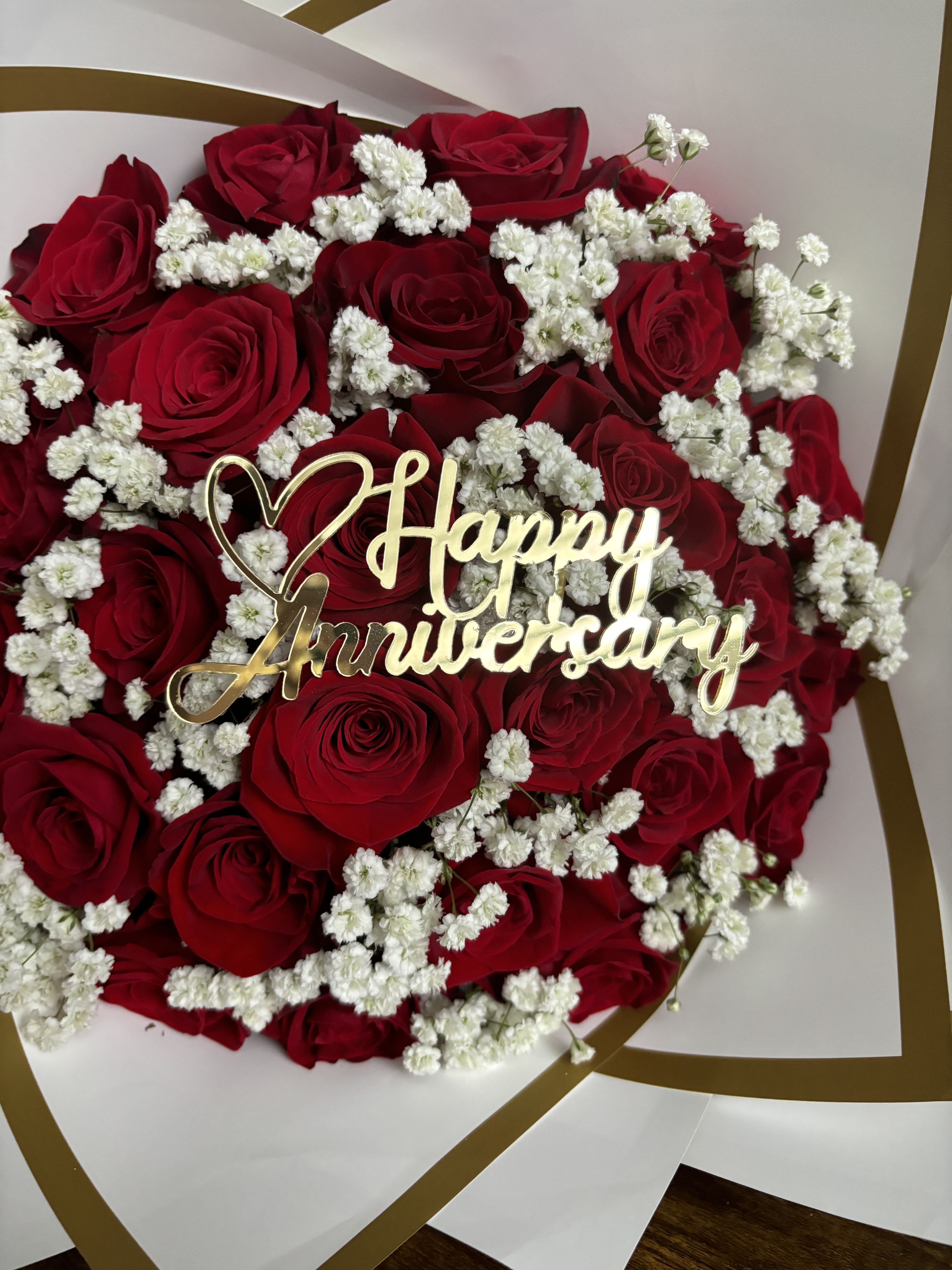 En Las Nubes Anniversary Bouquet - Celebrate love and lasting memories with our elegant Happy Anniversary Bouquet, featuring stunning red roses beautifully accented with baby’s breath. This classic arrangement symbolizes deep love, passion, and devotion—perfect for anniversaries, romantic surprises, or any special occasion that deserves a touch of timeless beauty.  Wrapped with sophistication and adorned with a golden “Happy Anniversary” topper, this bouquet is the perfect way to say “I love you” in the most unforgettable way.