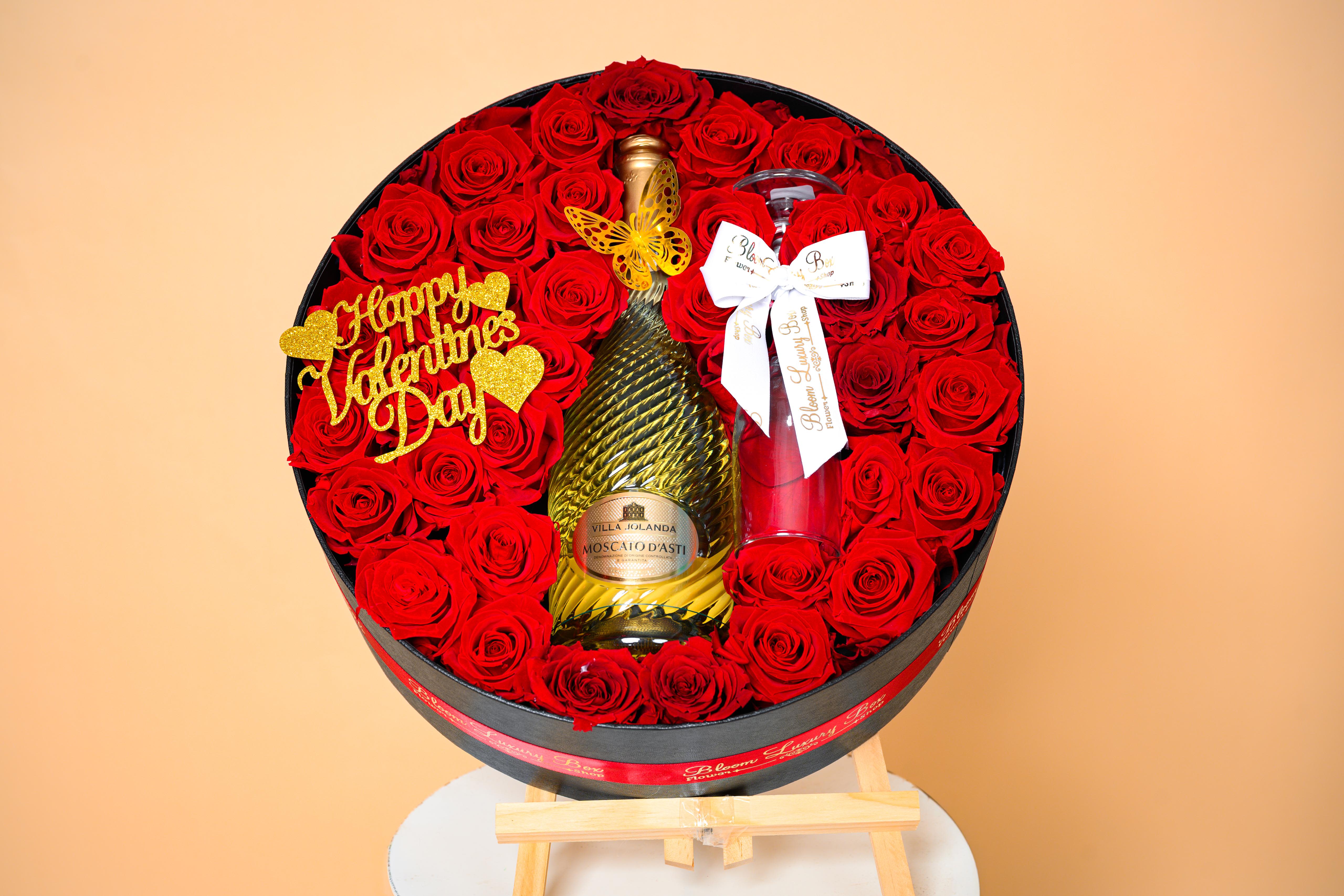 The Celebration of Love - This breathtaking round arrangement blends radiant red roses with a celebratory champagne centerpiece, framed by elegant Valentine accents and signature Bloom Luxury Box finishes. The Celebration of Love transforms romance into a luxurious experience.