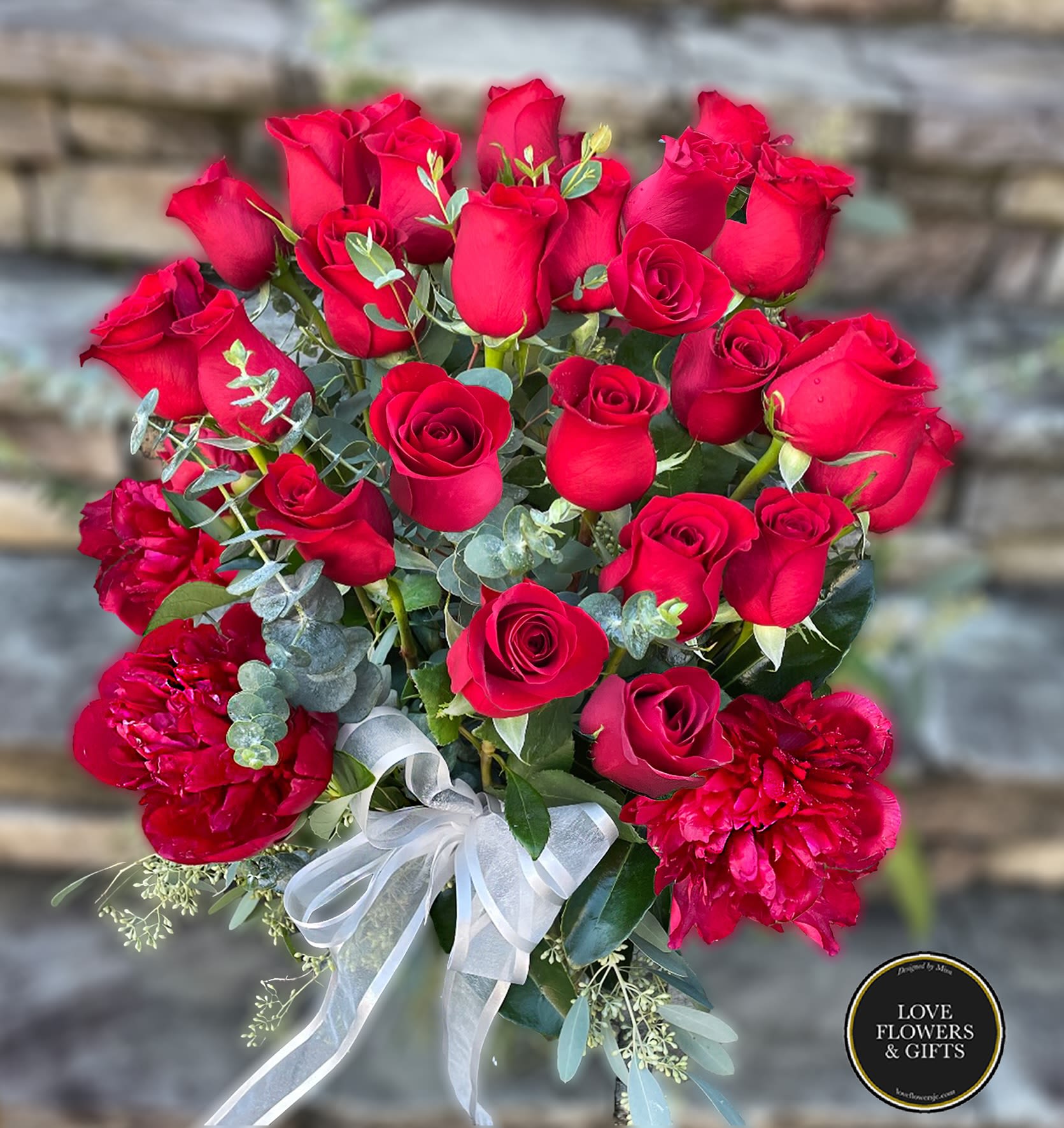 Tall arrangement of red roses and red peonies with a white bow