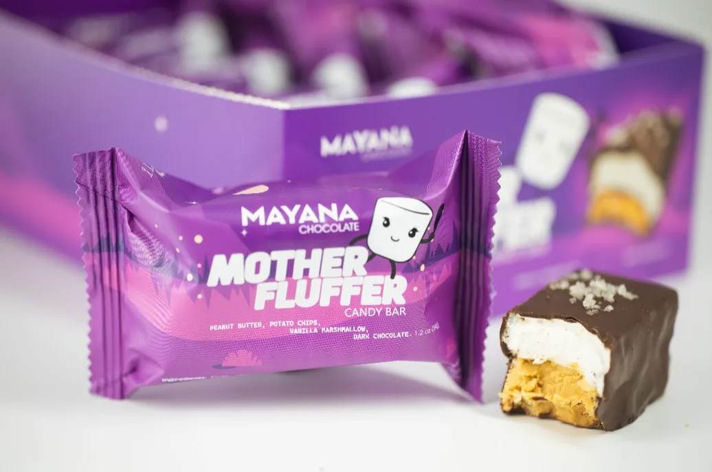 Mayana Mother Fluffer Bar - Mayana's NEW Mother Fluffer bar blends silky dark chocolate, creamy peanut butter, roasted white chocolate, crunchy potato chips, and a fluffy marshmallow layer. A sweet and salty explosion in every bite, an indulgent adventure for your taste buds. Dare to unwrap delight--your snack game will never be the same!  1.2 oz bar  Ingredients: Dark Chocolate (Cocoa Liquor, Cocoa Butter, Sugar, Soy Lecithin), Sugar, Peanut Butter (Peanuts, Salt, Responsibly Sourced Palm Oil), Roasted White Chocolate (Sugar, Cocoa Butter, Milk Powder, Vanilla, Soy Lecithin), Potato Chips (Potatoes, Vegetable Oil, Salt), Gelatin, Dextrose, Glucose Syrup, Vanilla Extract.  Contains: Peanuts, Milk, Soy.  May contain: Traces of tree nuts, eggs, and wheat. 