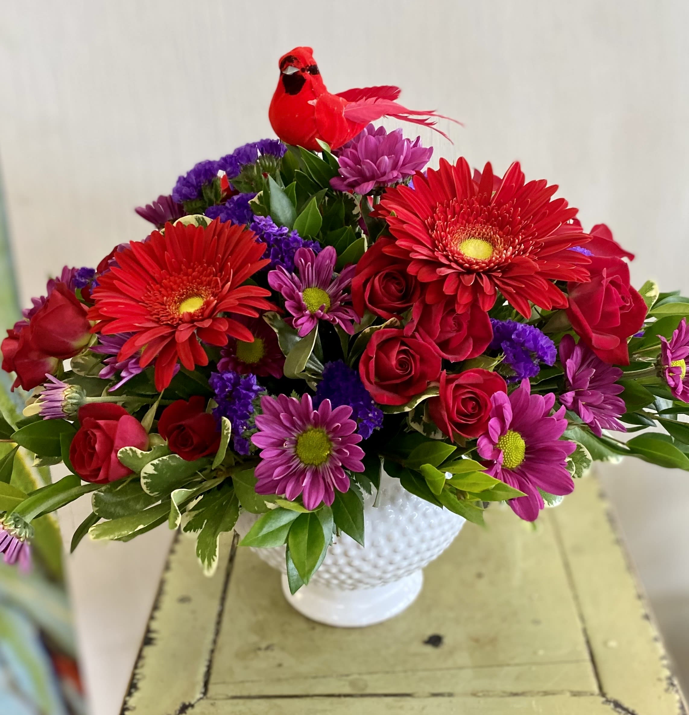 Cardinals Mean Love - The saying goes that spotting a Cardinal  means a loved one is near. A bright red Cardinal sits atop a bed of jewel tone flowers, all arranged in a pretty hobnail ceramic container. 