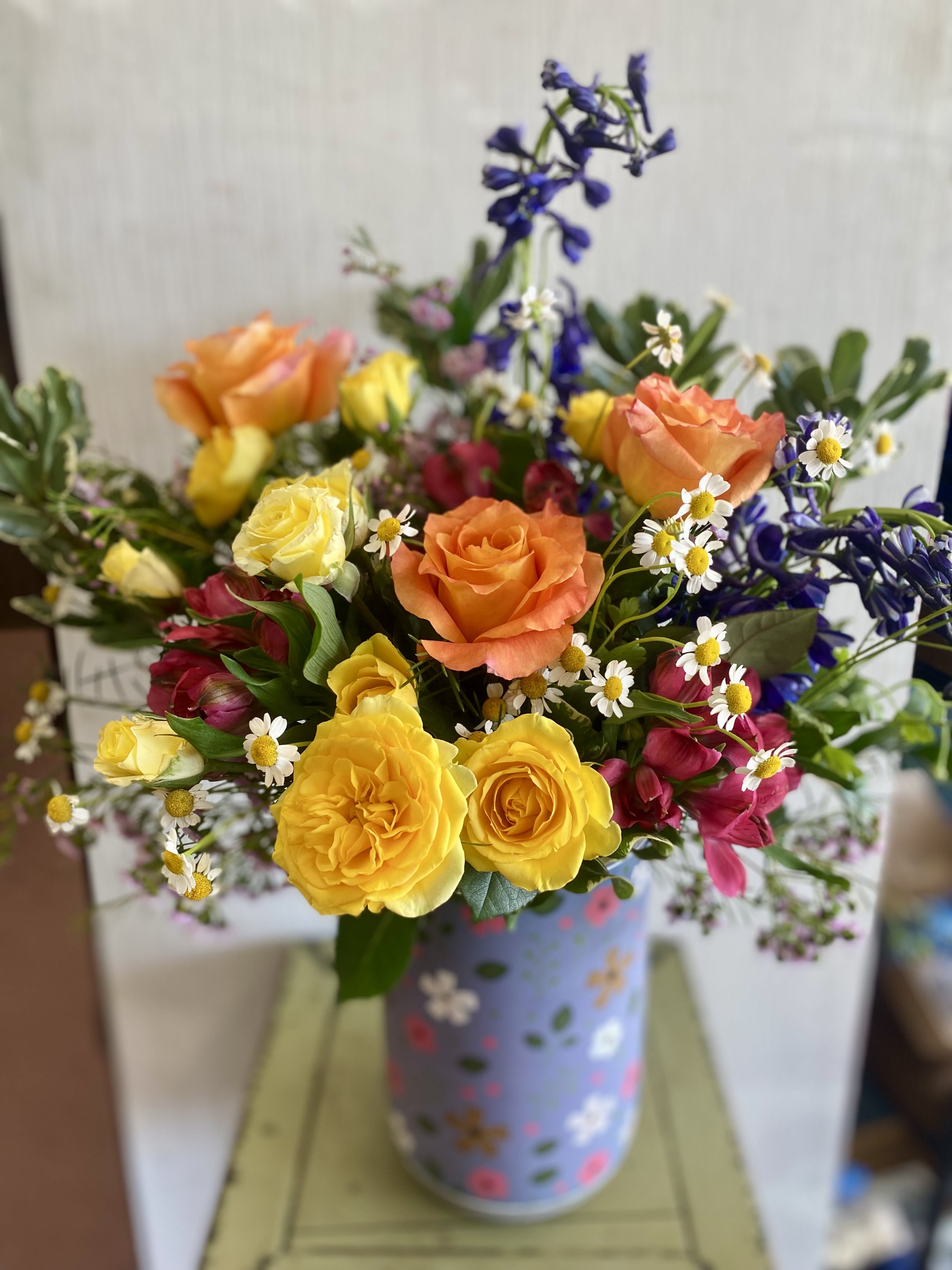 Happy Heart  - Good vibes and sunshine abound! Bright and cheery colors shine in this lush arrangement featuring roses and delphinium surrounded by premium foliage and complementary flowers. The vase is special ... floral embossed ceramic in three colorways: blue, green, and pink. 