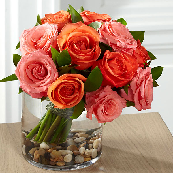The FTD Blazing Beauty Rose Bouquet - Blooming with grace and style this stunning rose bouquet is set to send warm wishes to your recipient in way that will lift their spirits and have them delight in the unexpected. Salmon roses and coral roses combine to create a bright blushing display accented with lush greens and hand-tied to provide a rounded and full form. Casually placed in a large clear glass cylinder vase with river rocks at the bottom to create even further interest this fresh floral arrangement will be an unforgettable birthday thank you or Mother's Day gift. GOOD bouquet includes 12 stems. Approx. 8"H x 8"W. BETTER bouquet includes 16 stems. Approx. 9"H x 8"W. BEST bouquet includes 20 stems. Approx. 11"H x 8"W.