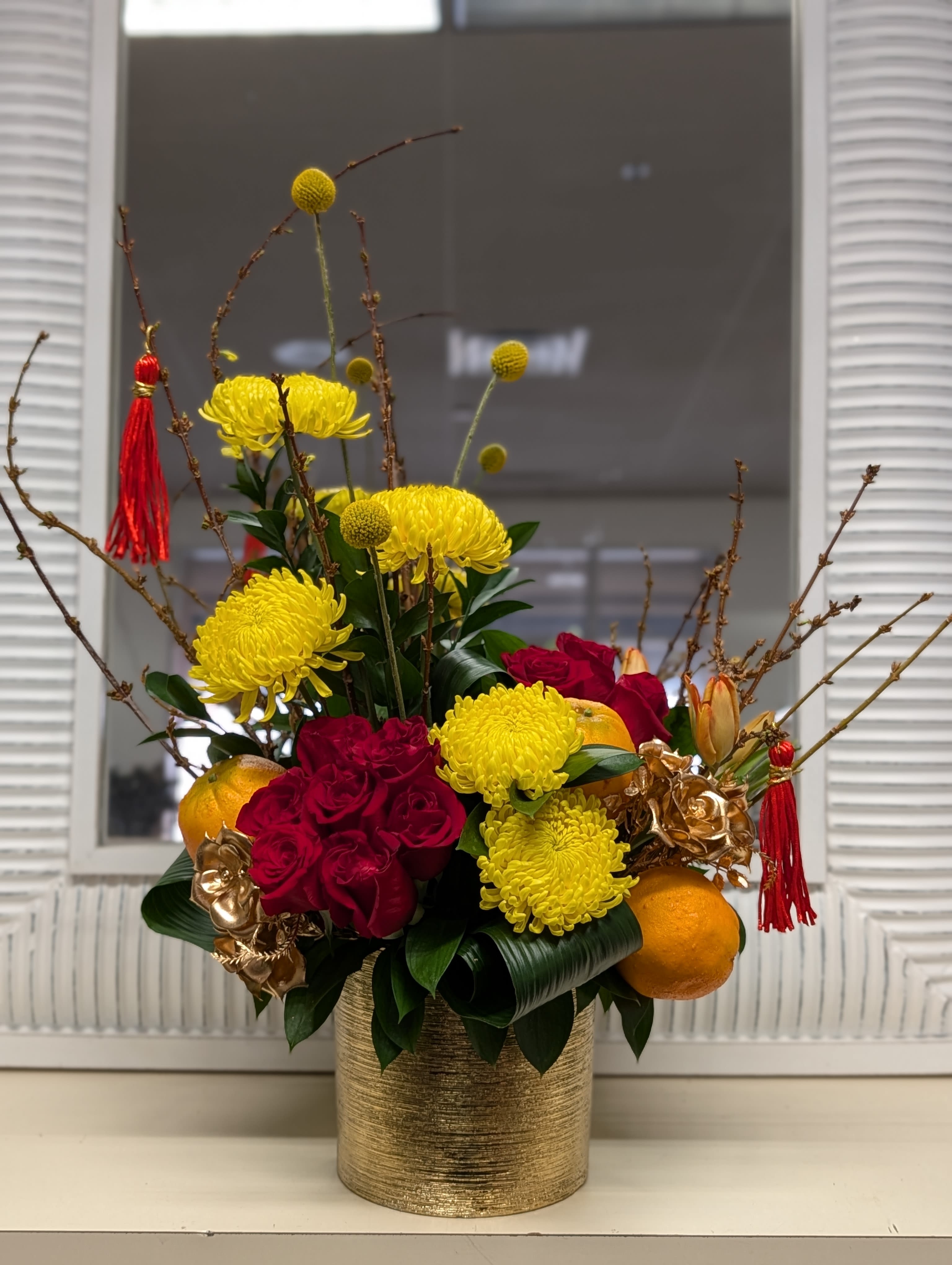 Chinese New Year - This beautiful arrangement of red roses, yellow chrysanthemum, faux oranges, blooming branch (seasonal maybe sub) design in a etched gold ceramic vase. 
