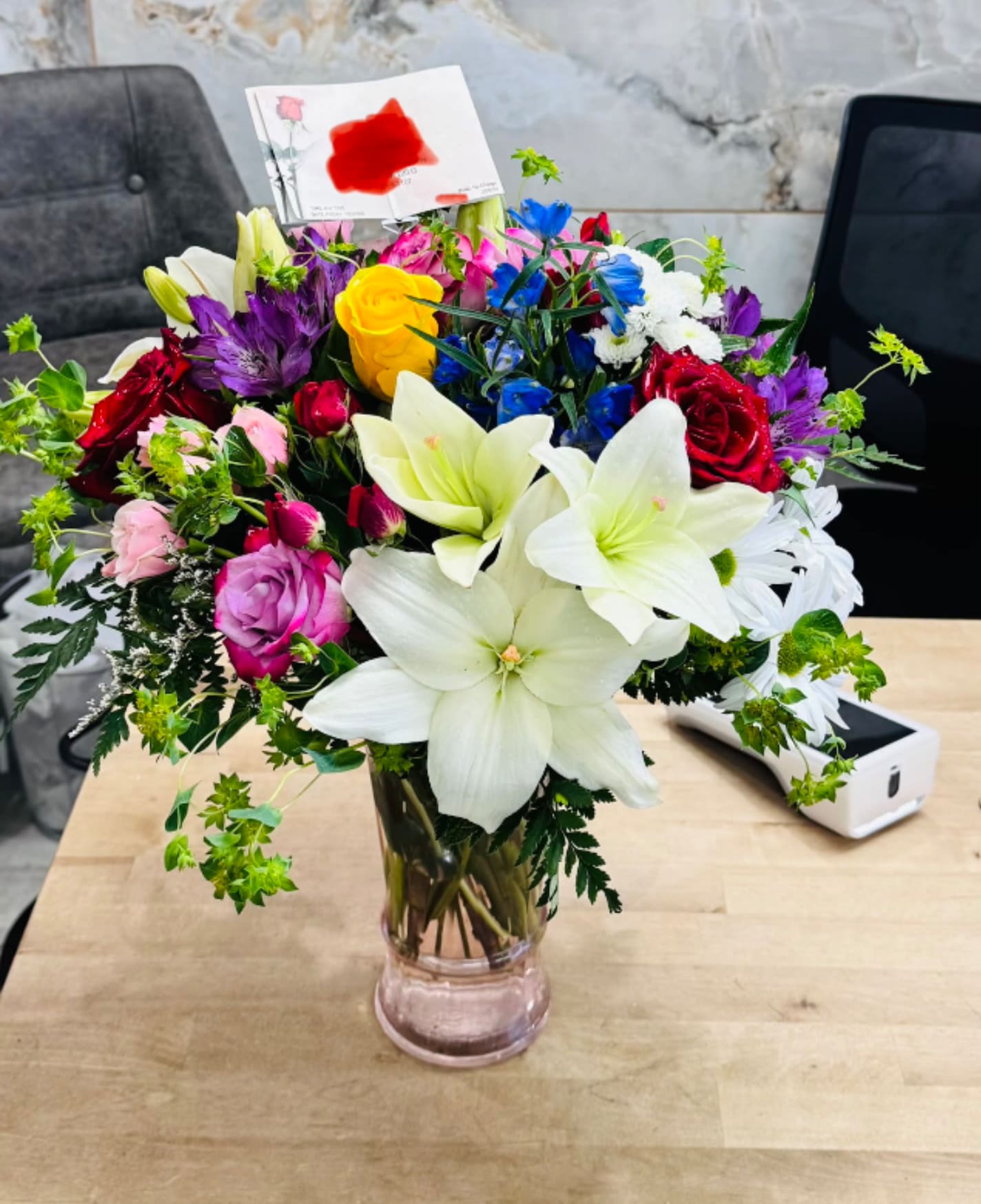 Luminous Harmony - A vibrant fusion of texture and color, this lush bouquet blends ivory lilies with ruby roses, cobalt delphiniums, and pops of pink and yellow. Fresh greenery and delicate filler blooms weave through the arrangement, creating a sculpted yet organic silhouette. Perfect for sophisticated events or a refined centerpiece, it exudes elegance, joy, and timeless charm.