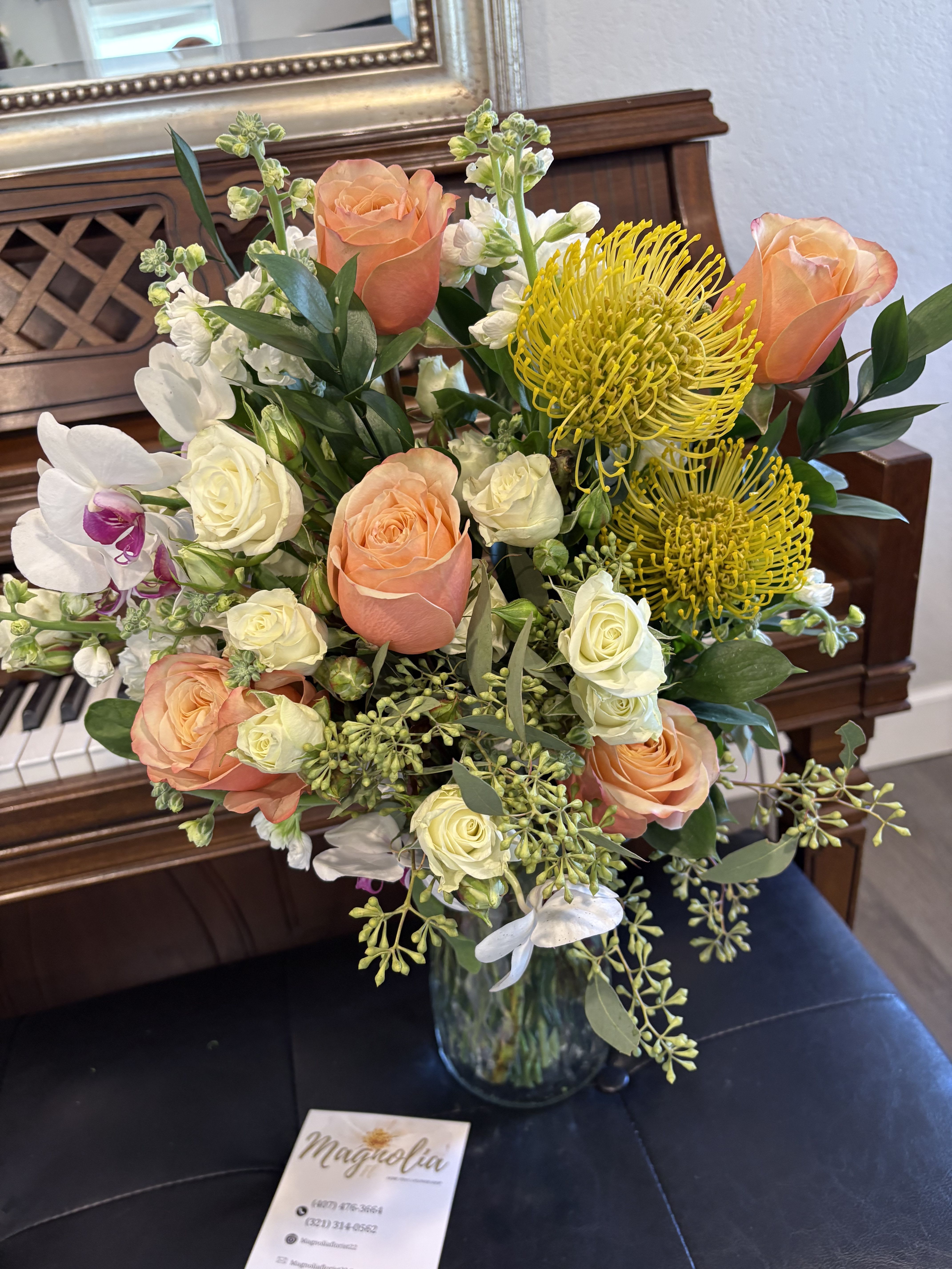 Vibrant Elegance Bouquet - This exquisite floral arrangement showcases peach and creamy white roses paired elegantly with yellow pincushion proteas and exotic white orchids accented with pink tones. Enhanced by lush green leaves, this bouquet exudes freshness and sophistication, making it a perfect centerpiece for any elegant setting.