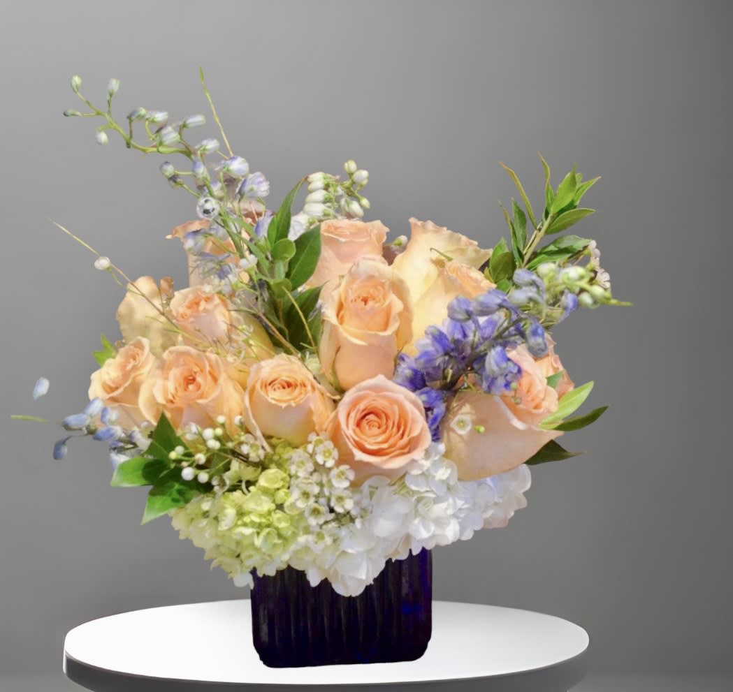 Peachy - A sweet and delicate arrangement of peach roses, hydrangea, delphinium, and seasonal foliage in a glass vase. A beautiful way to say Happy Mother's Day, welcome a new baby, or brighten someone's day.