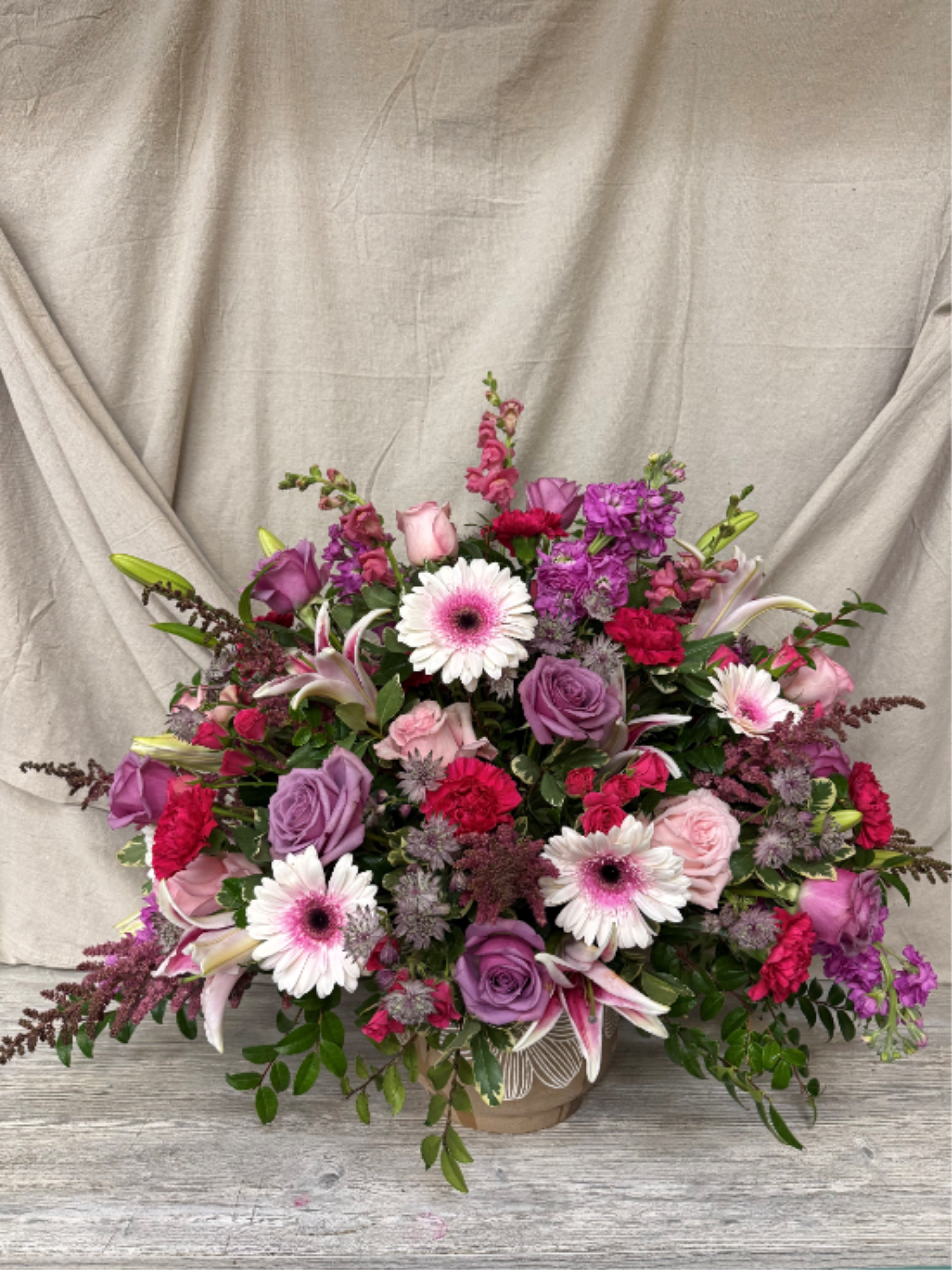 Rose Quartz Bloom - This stunning large floral arrangement is a lush celebration of pinks and purples, designed to make a statement from every angle. A generous mix of premium blooms—layered with soft blush tones, rich magentas, and velvety violets—creates depth, movement, and undeniable romance. Accented with fresh greenery and thoughtfully styled for fullness, each flower complements the next for a look that’s both elegant and vibrant. Perfect for milestone celebrations, grand gestures, or simply filling a space with beauty, this arrangement feels abundant, expressive, and effortlessly luxurious.