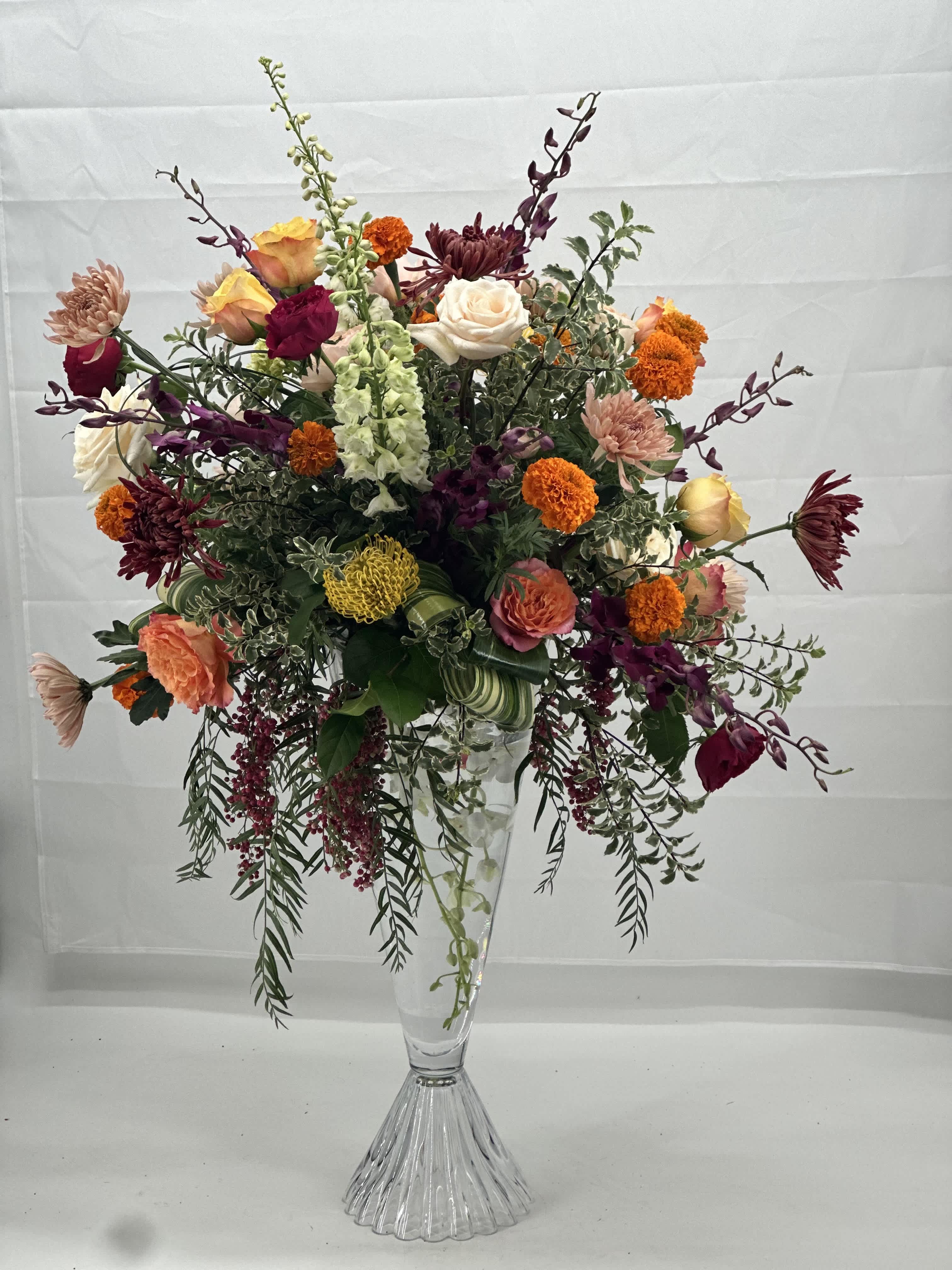 Velours Botanical  - This is a Tall floral arrangement with very generous ,editorial presence -artful ,abundant ,and intentionally  wild while still feeling composed. The arrangement is vertical and airy ,designed with generous negative space and movement.It feels European harden -inspired, sophisticated rather than tight or synthetical .The height and asymmetry  immediately signal luxury and confidence. Layered with muted sage and forest greens 